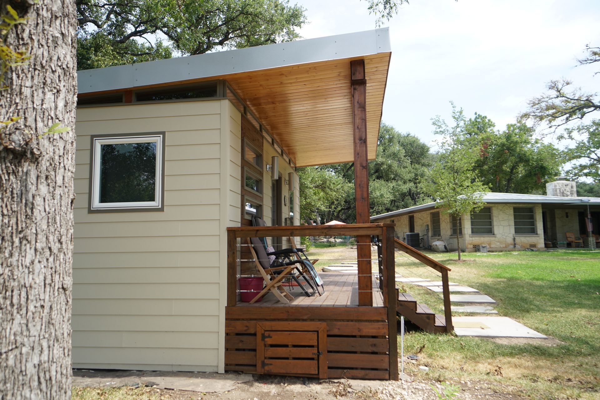 Small cabin with a wooden porch, built into the side of a larger building in a grassy area.