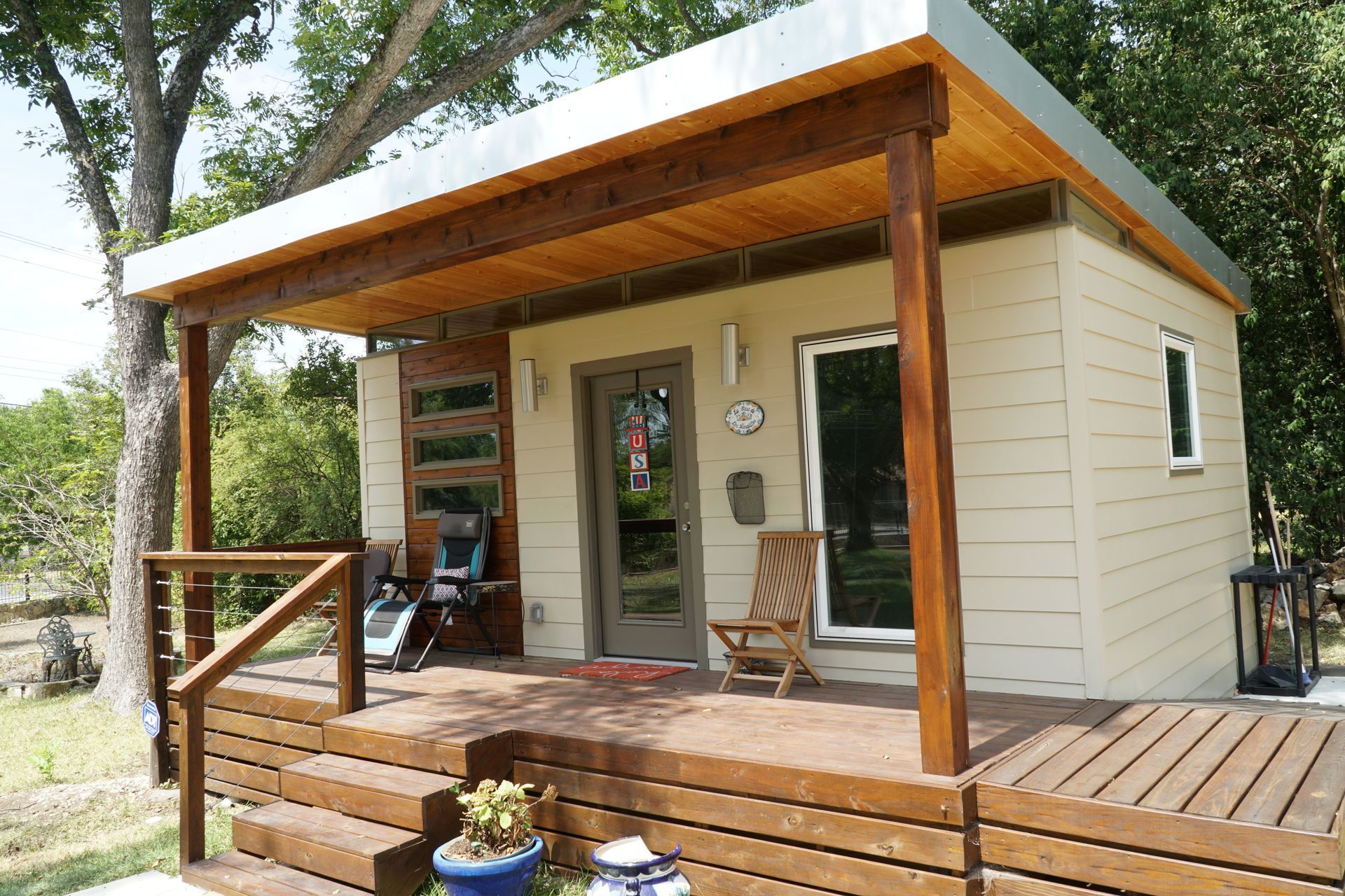 Tan modern tiny house with a wooden porch and a flat roof.
