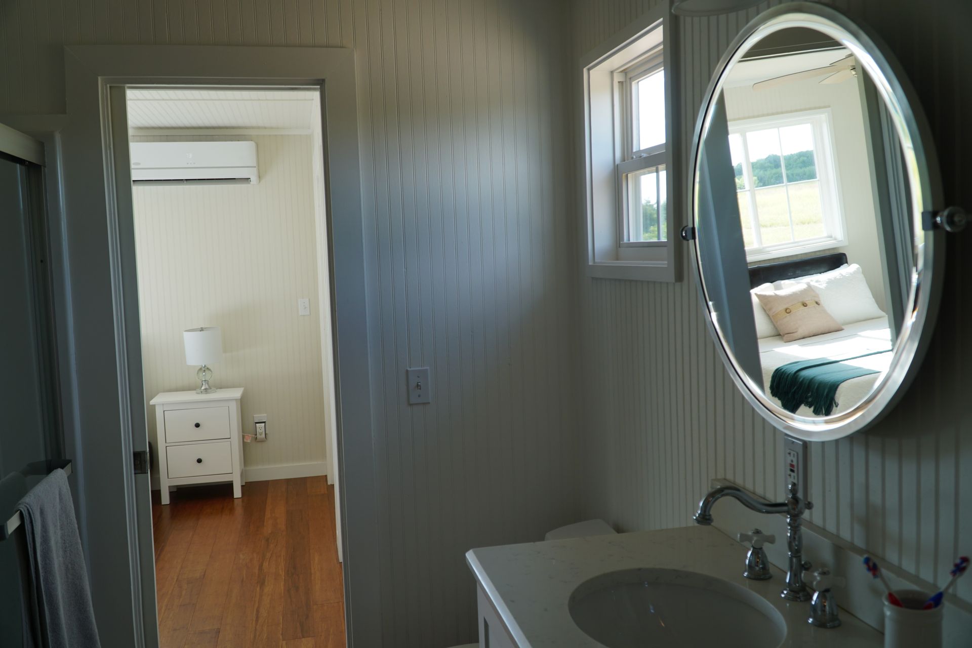 Bathroom with mirror, sink, and open doorway to a bedroom with bed and bedside table.