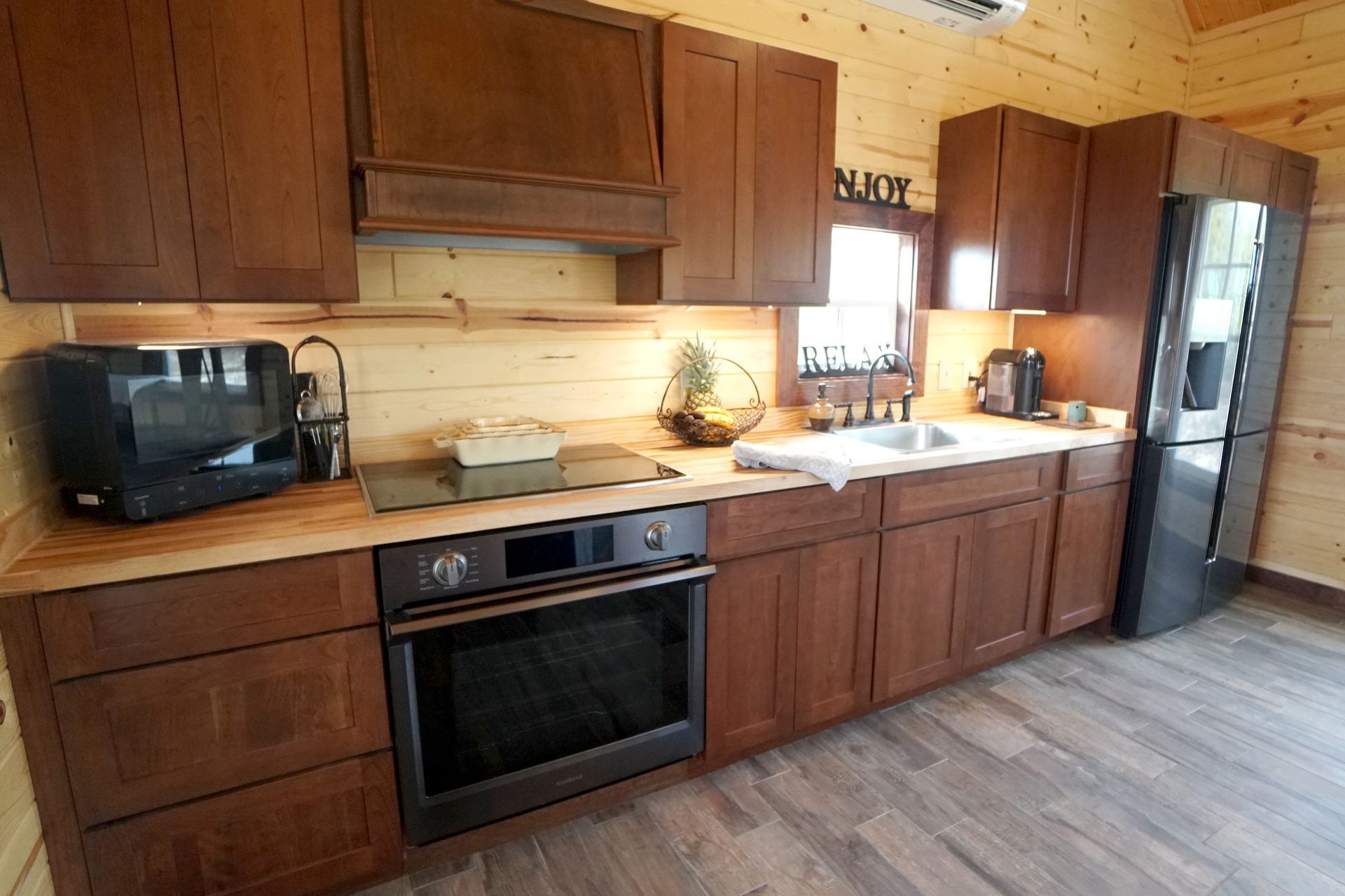 Kitchen with brown cabinets, stainless steel appliances, and wooden countertop in a cabin setting.