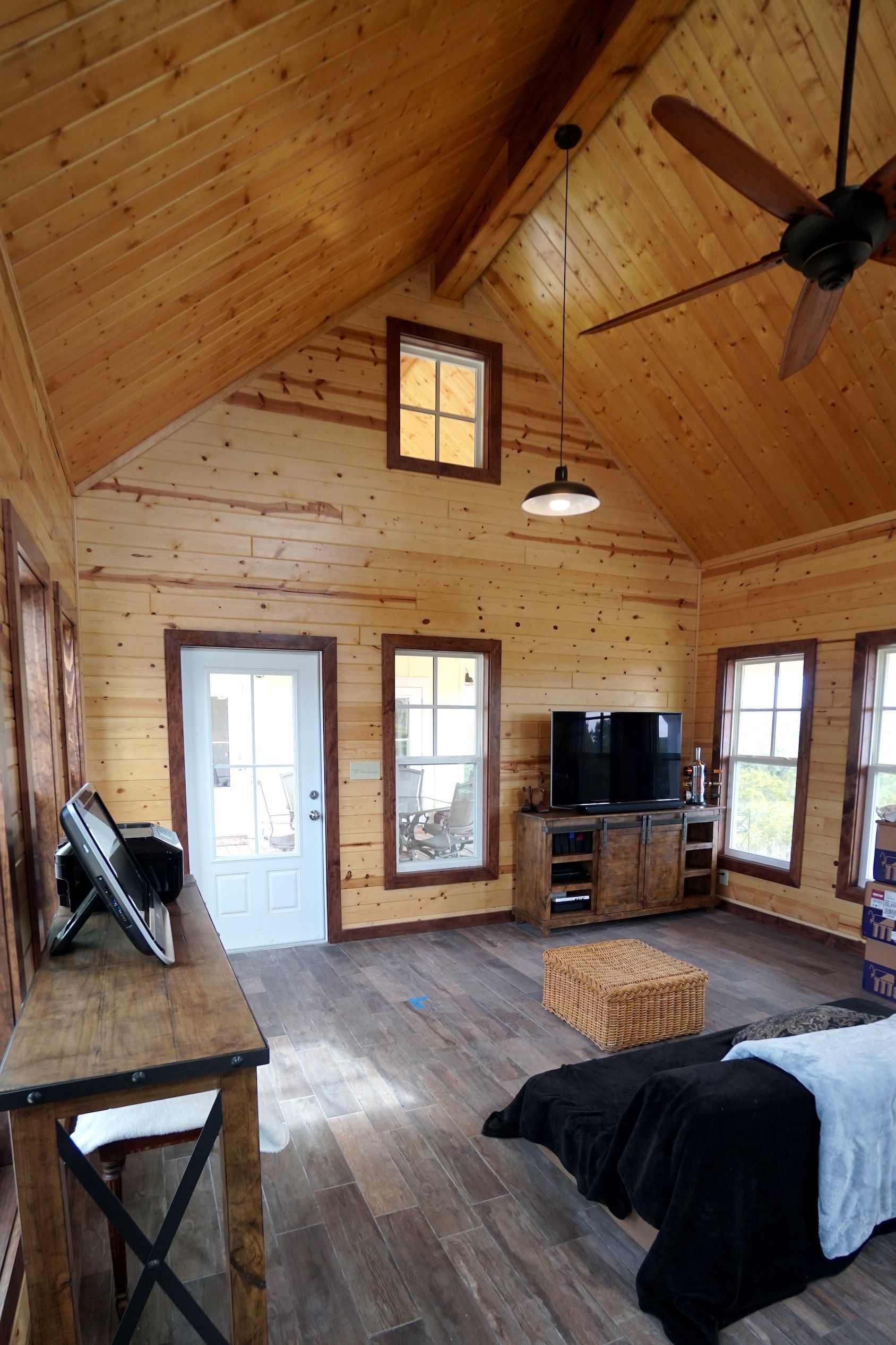 Cozy cabin interior with wood paneling, windows, and a bed. Sunlight streams across the floor.