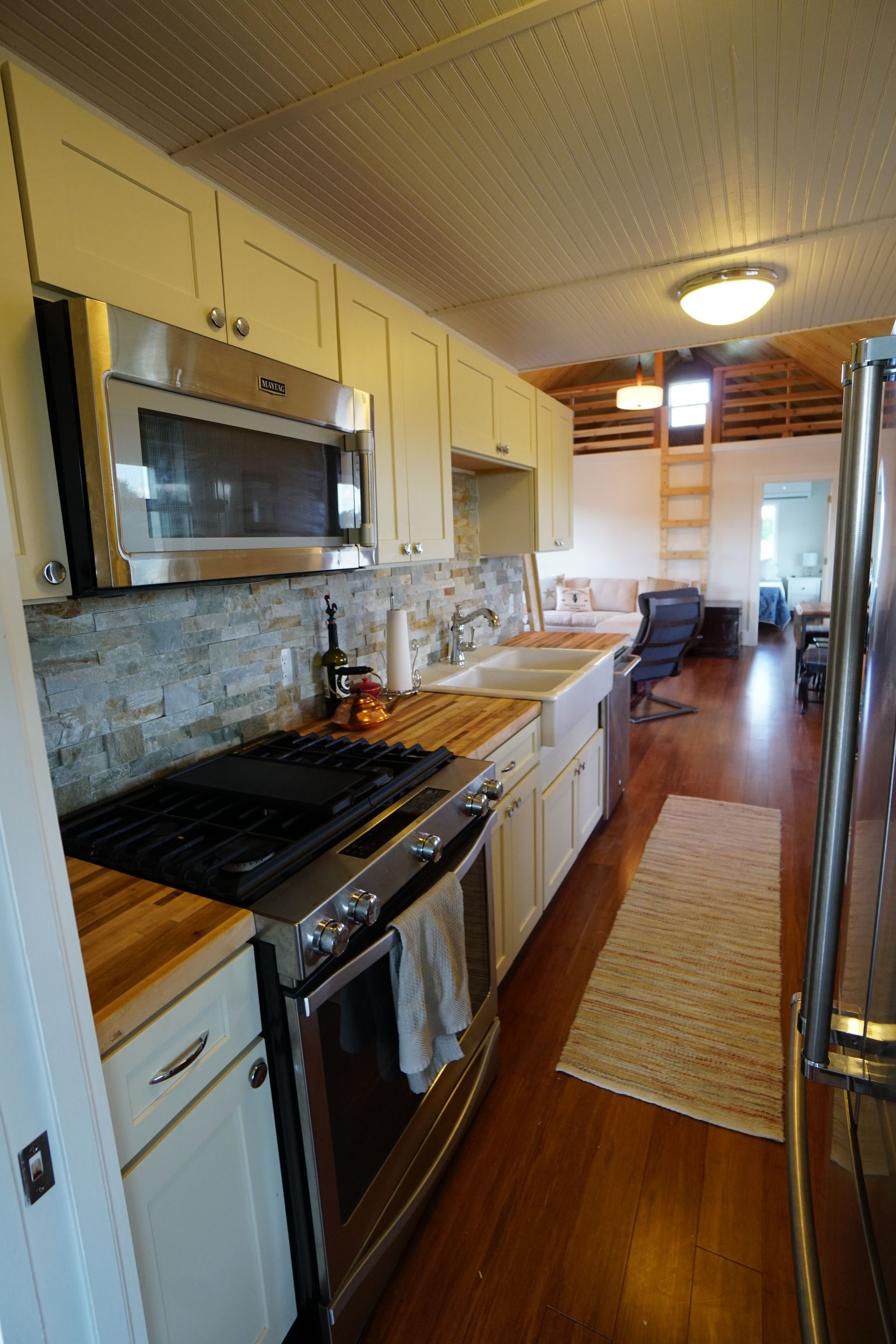 Long, narrow kitchen with stainless steel appliances, light cabinets, and butcher block countertops.