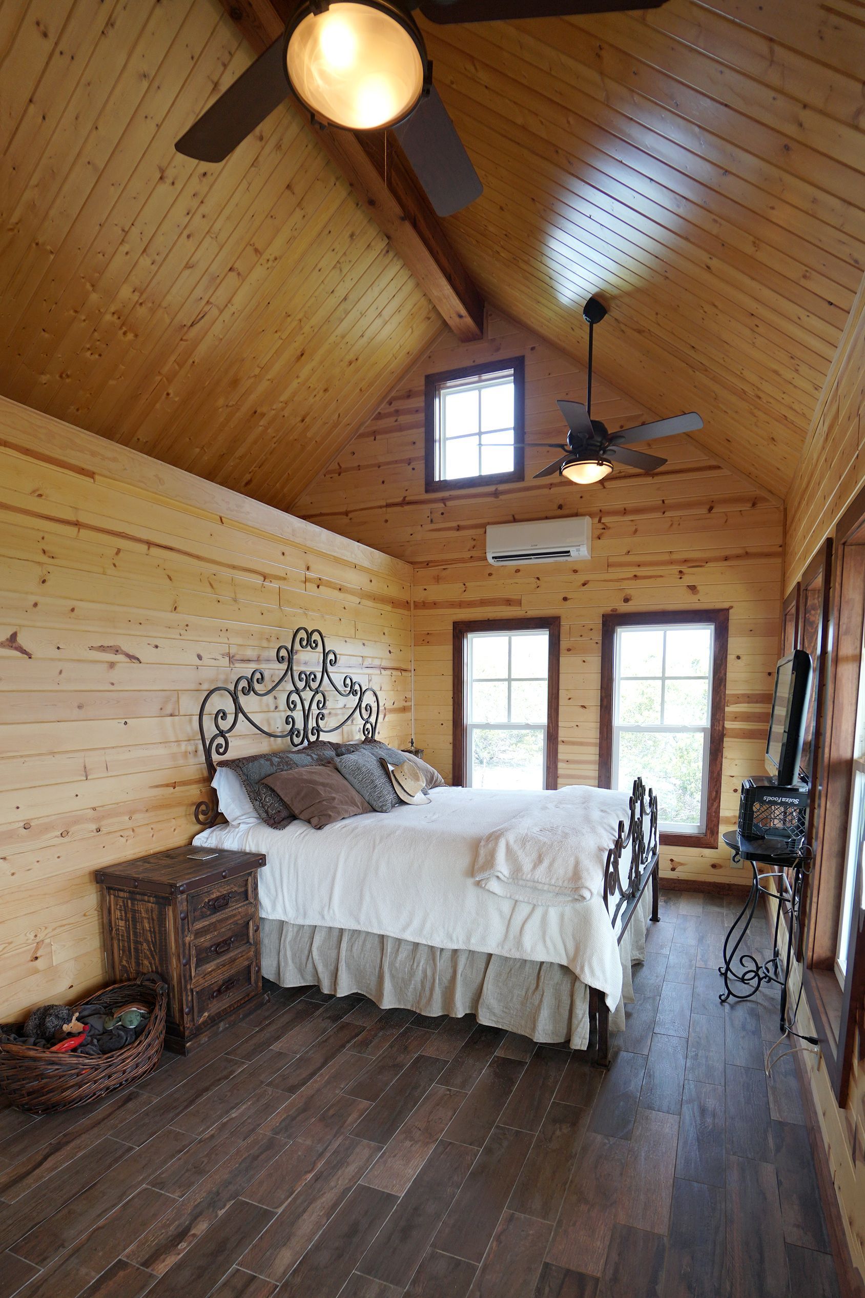 Bedroom with wood walls, vaulted ceiling, bed, nightstand, and windows.