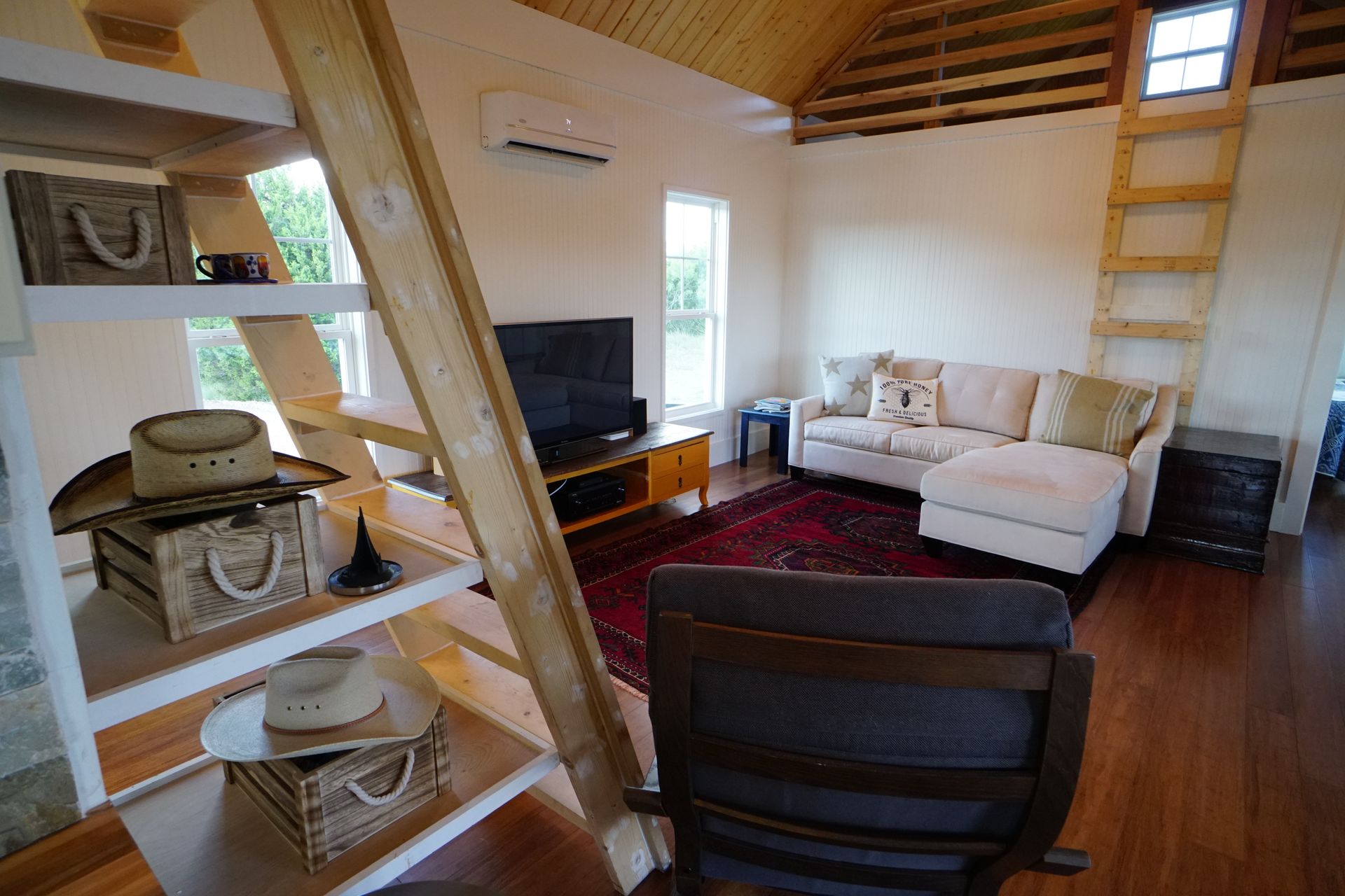 Cozy living room with white couch, TV, and wooden ladder leading to a loft.
