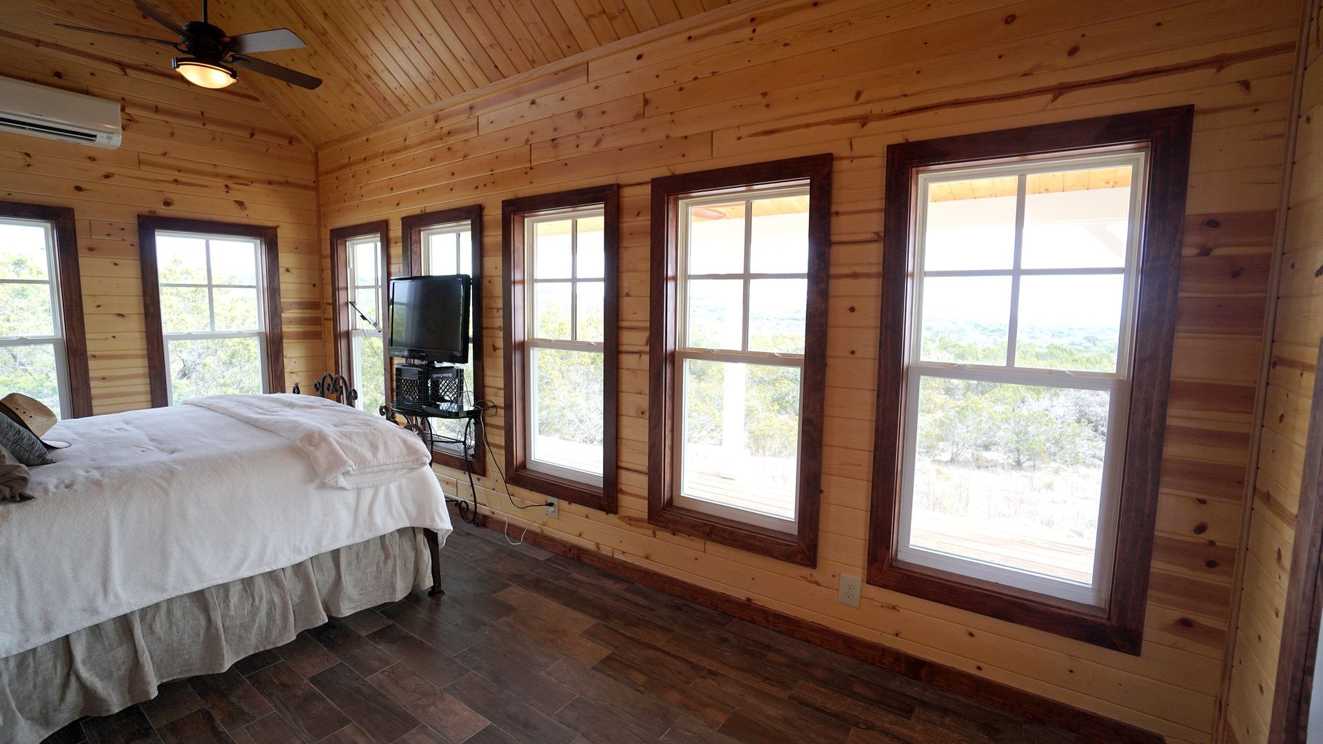Bedroom with wood walls, large windows, and a bed.