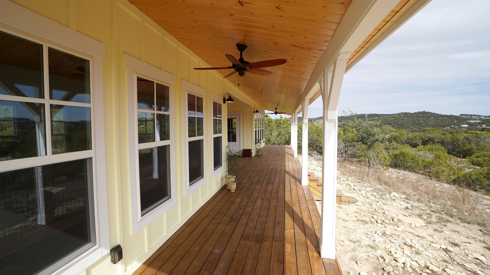Yellow house porch with windows, wooden deck, and a view of trees and sky.