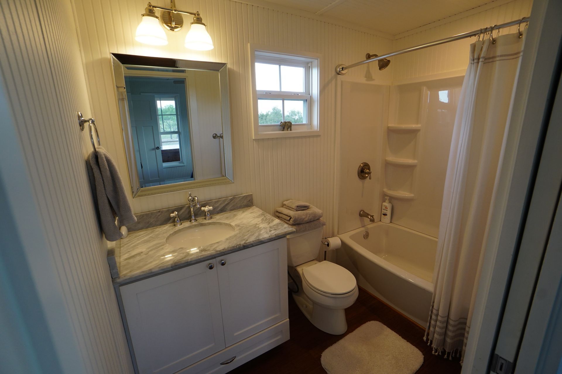 Bathroom with white vanity, toilet, and bathtub. Light-colored walls, small window, and a gray towel.