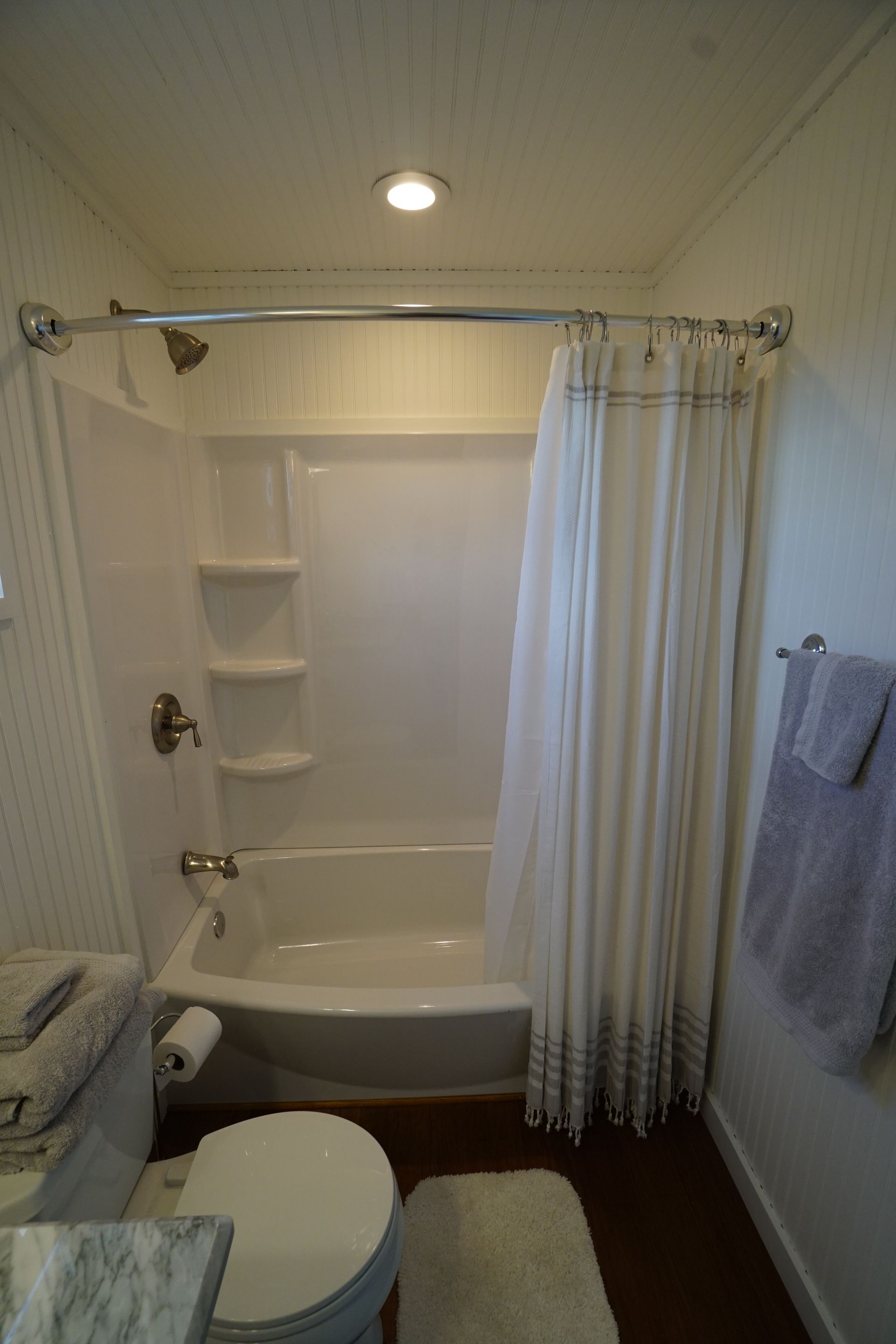 Bathroom with white shower/tub, curtain, toilet, towels, and rug.