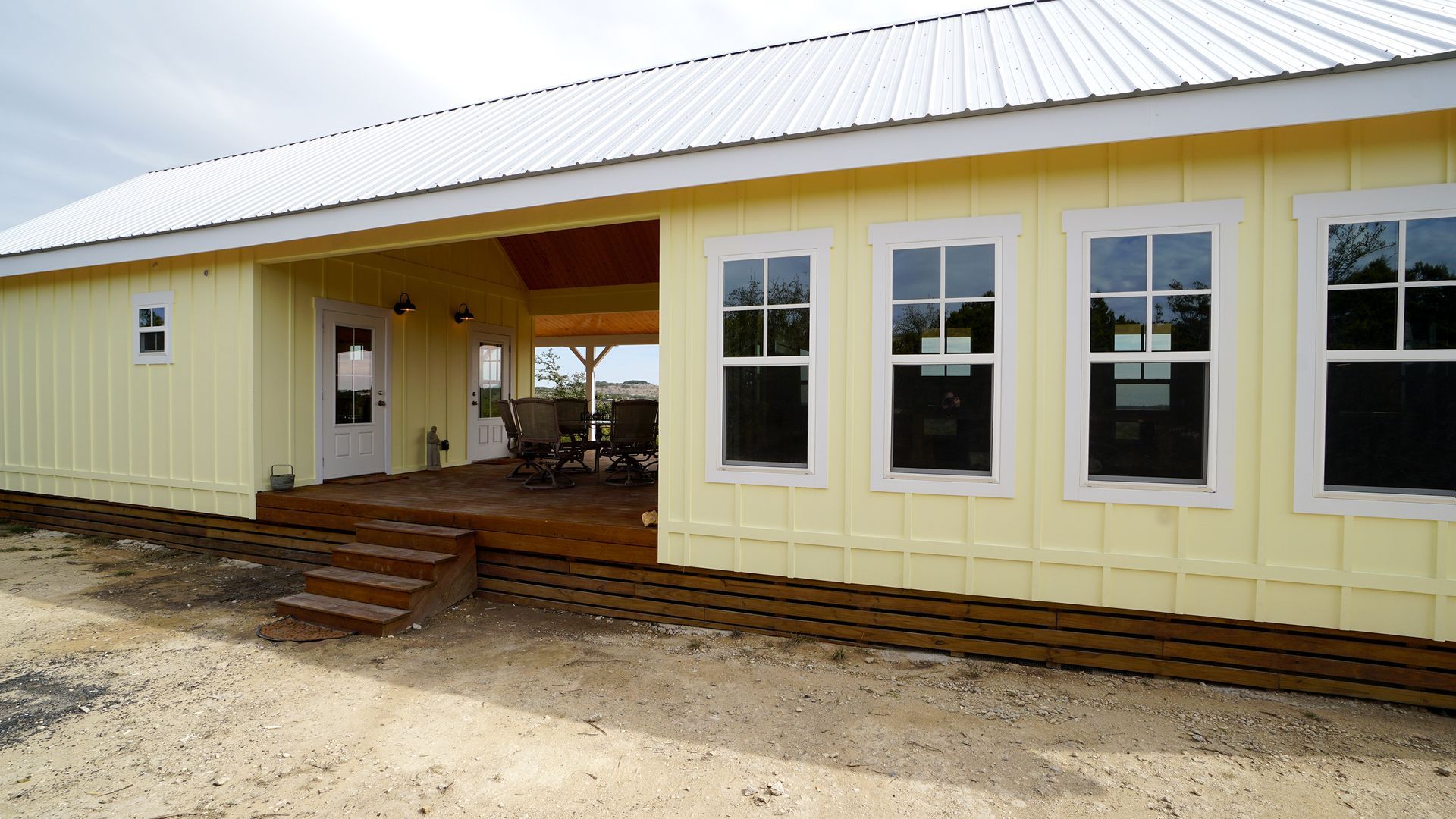 Yellow house with a porch and three windows, metal roof, wooden steps, and a cloudy sky.