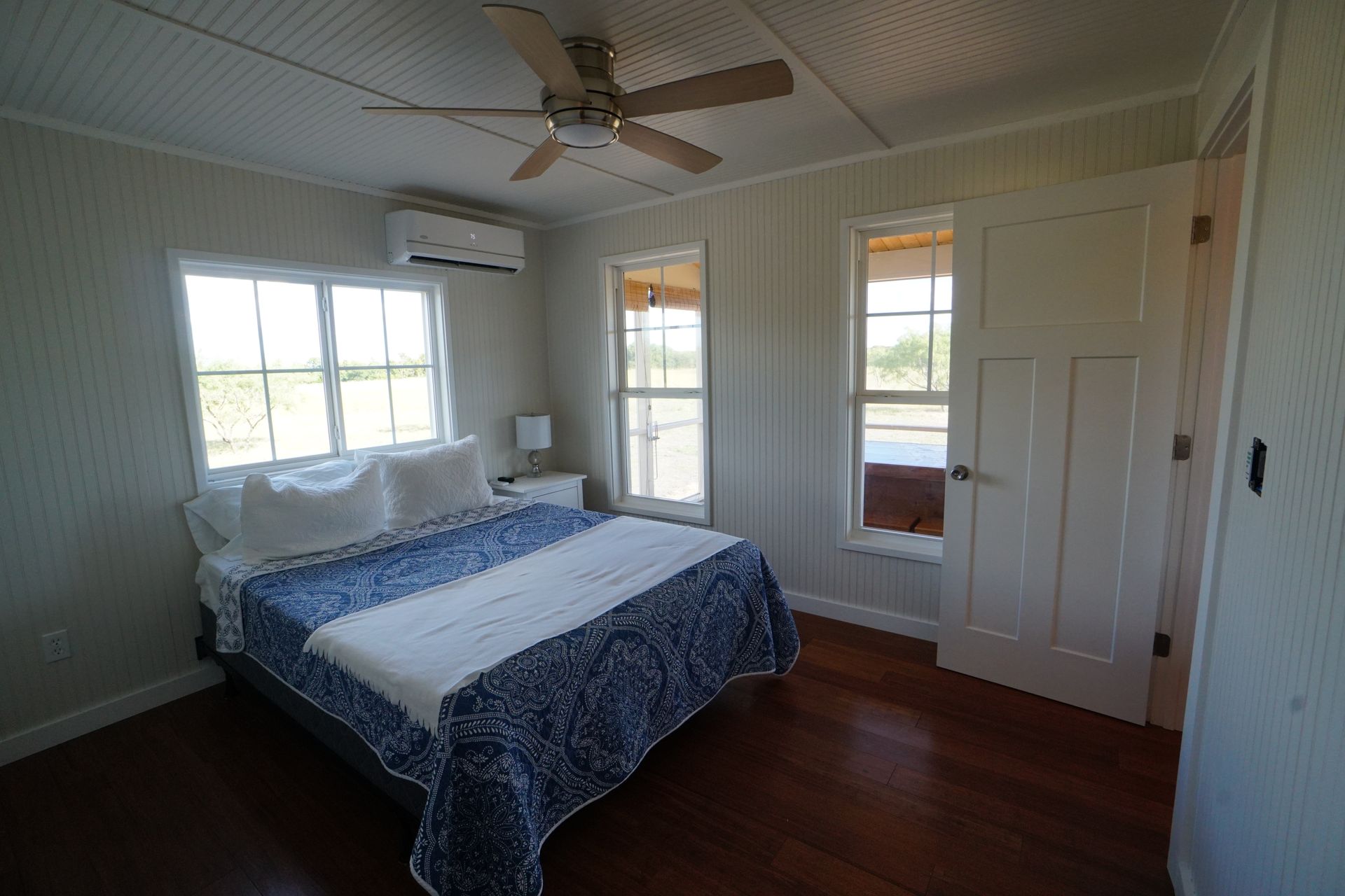 Bedroom with bed, windows, and ceiling fan. White walls, wood floor, and blue and white bedding.