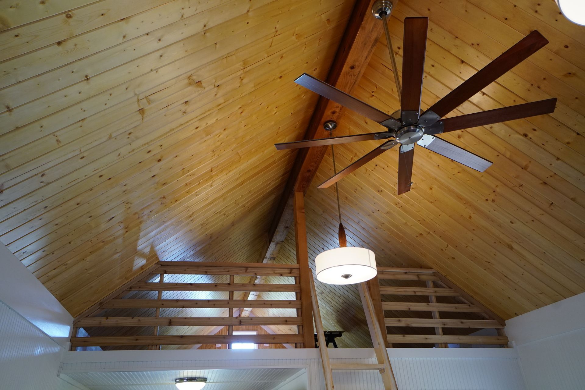 Wooden ceiling with a large ceiling fan and a loft with a railing and ladder.