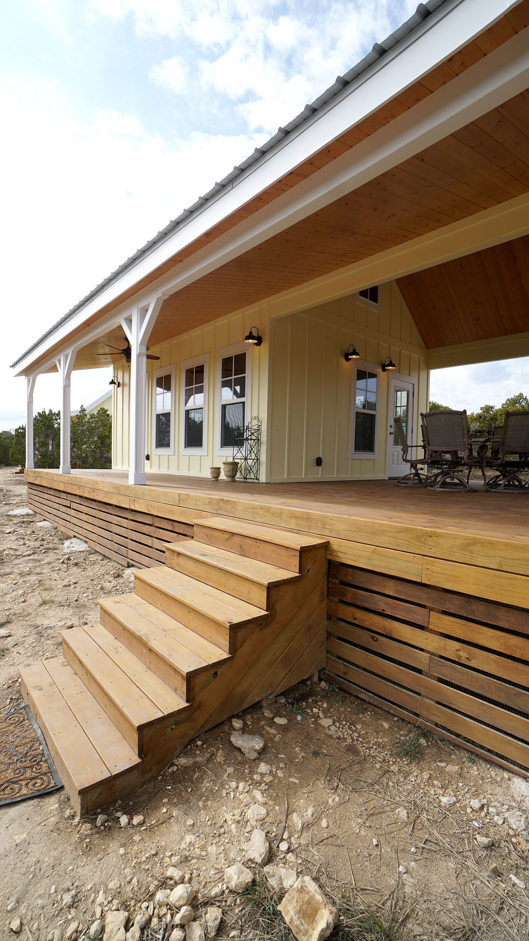 Wooden steps lead up to a light-yellow building with a long porch; the roof is white.
