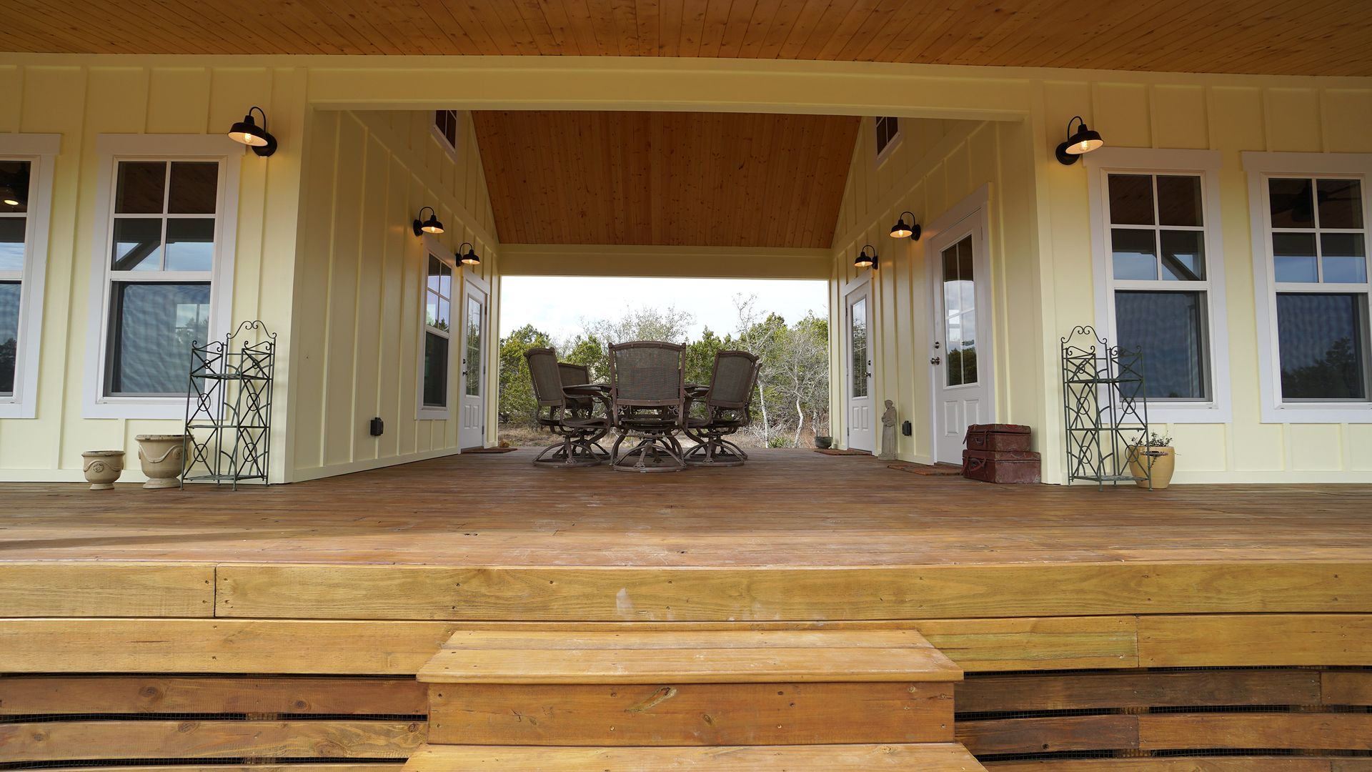 Yellow farmhouse porch with wooden deck, steps, and outdoor dining area.