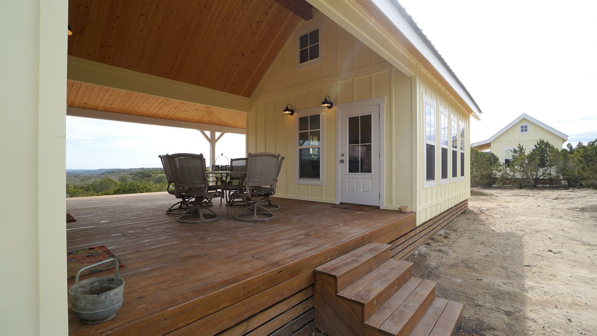Yellow house with deck overlooking landscape. Deck features table, chairs, and steps.