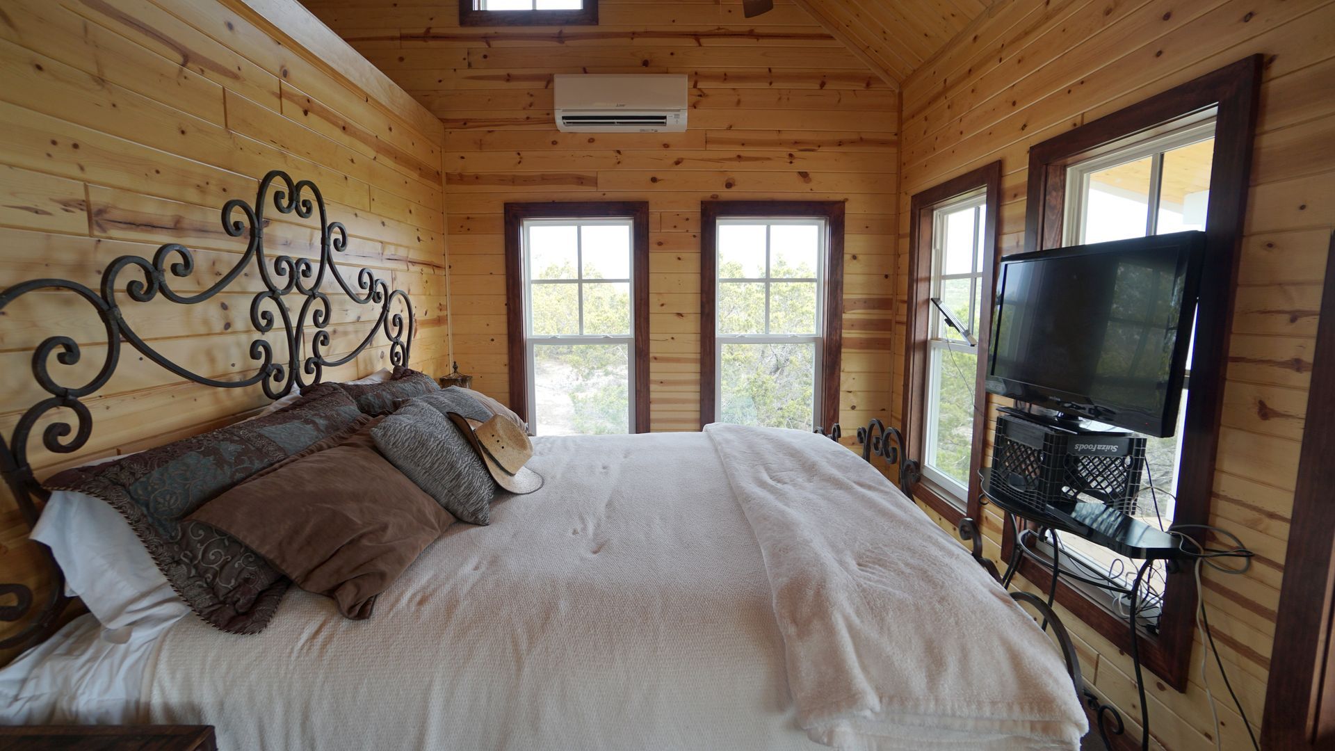 Bedroom with wood-paneled walls, wrought-iron bed frame, large bed with pillows, and a mounted TV.