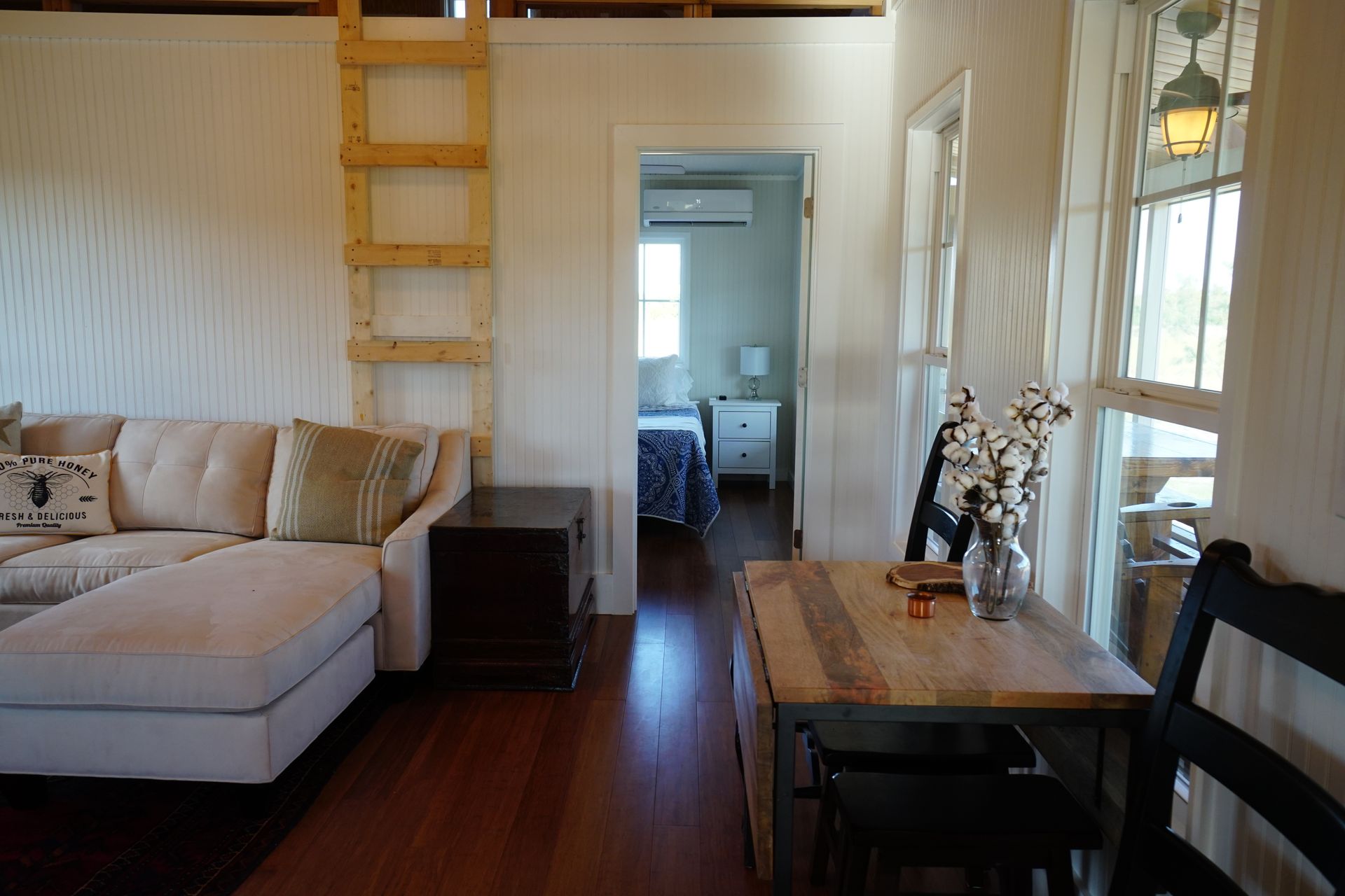Cozy cabin interior with a couch, table, and bedroom visible in the doorway. Wooden ladder leads up.