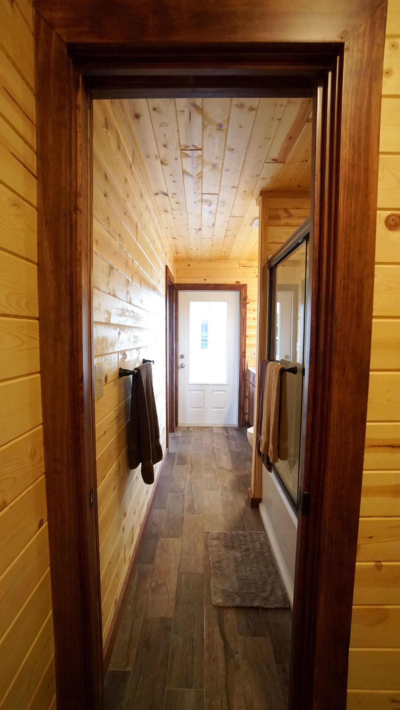 Doorway to a hallway with wooden walls and ceiling. Door at end, towels and bath in sight.