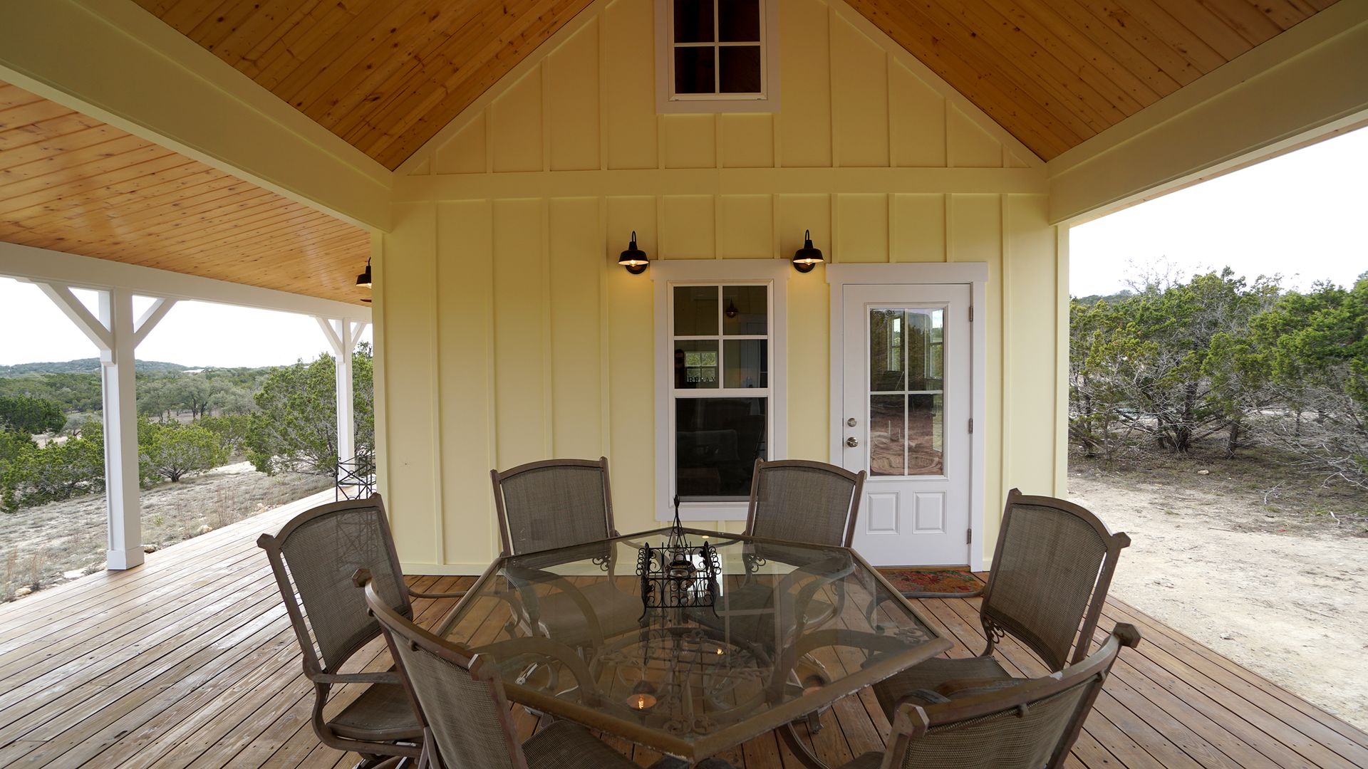 Covered patio with yellow siding, wooden deck, glass-top table, and six chairs.