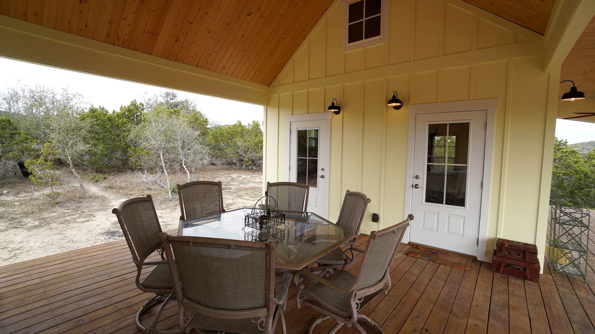 Yellow porch with glass table, chairs, white doors, and wooden ceiling.