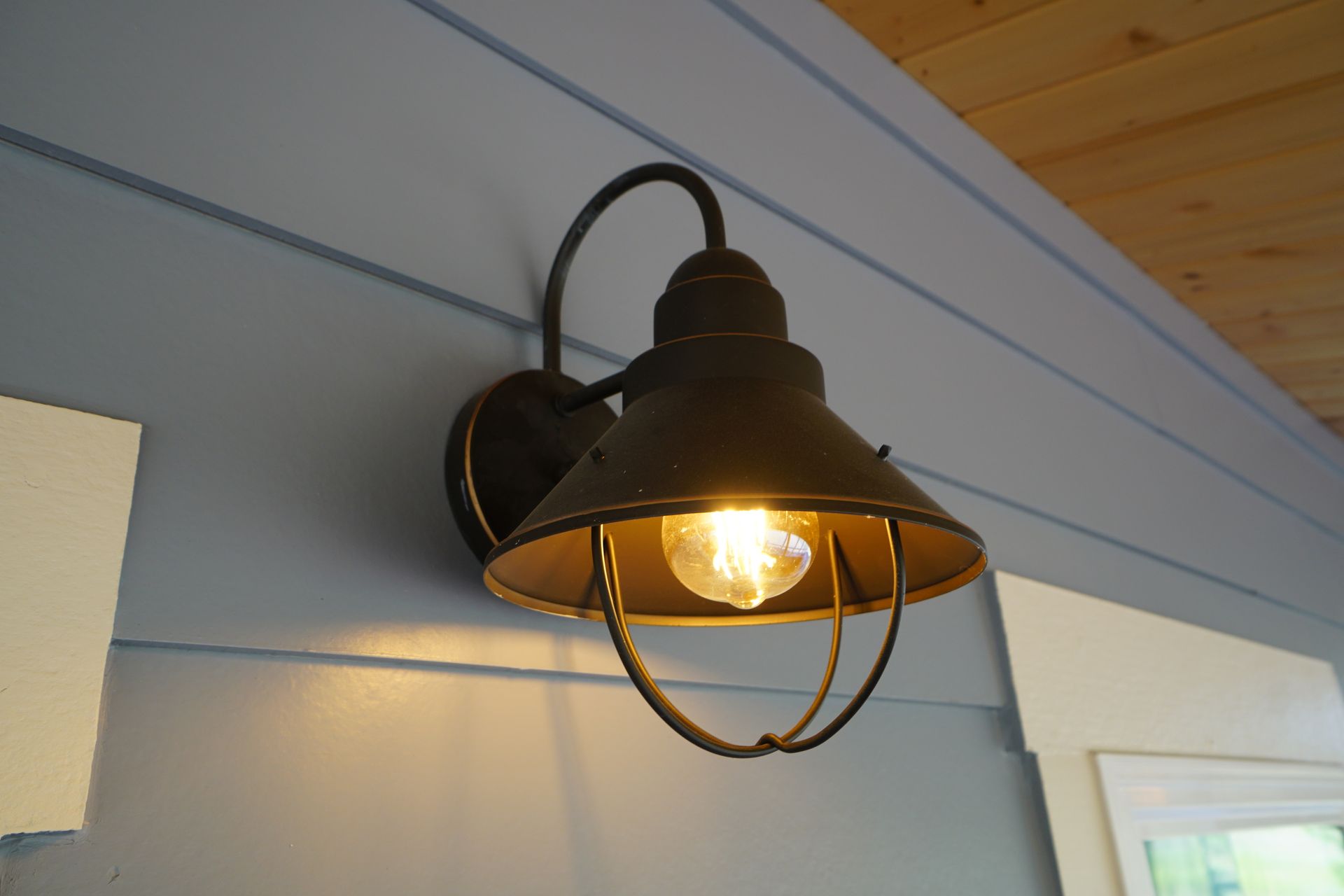 Black outdoor wall-mounted light fixture with a caged shade, mounted on a blue wall.