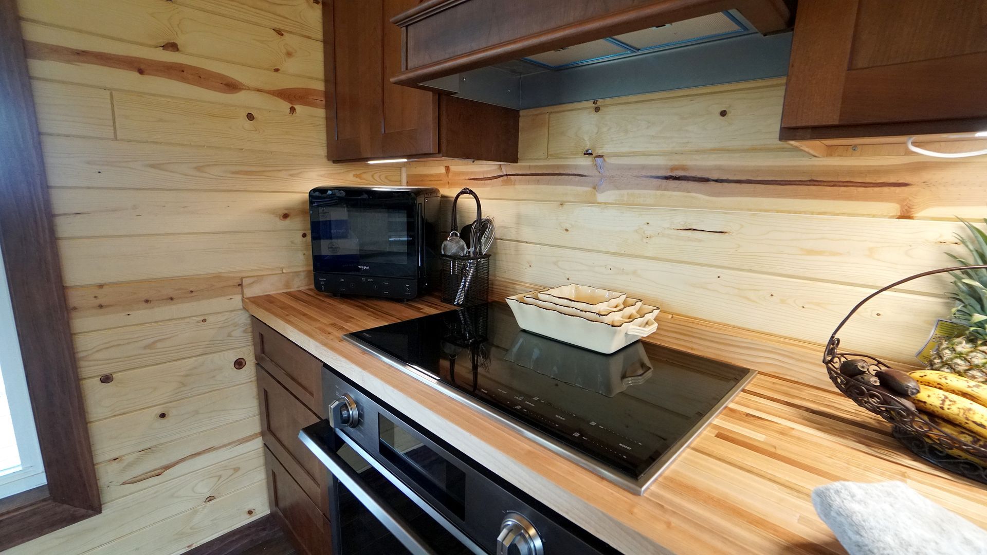 Kitchen with wooden cabinets and walls, featuring a stovetop, oven, microwave, and decorative elements.