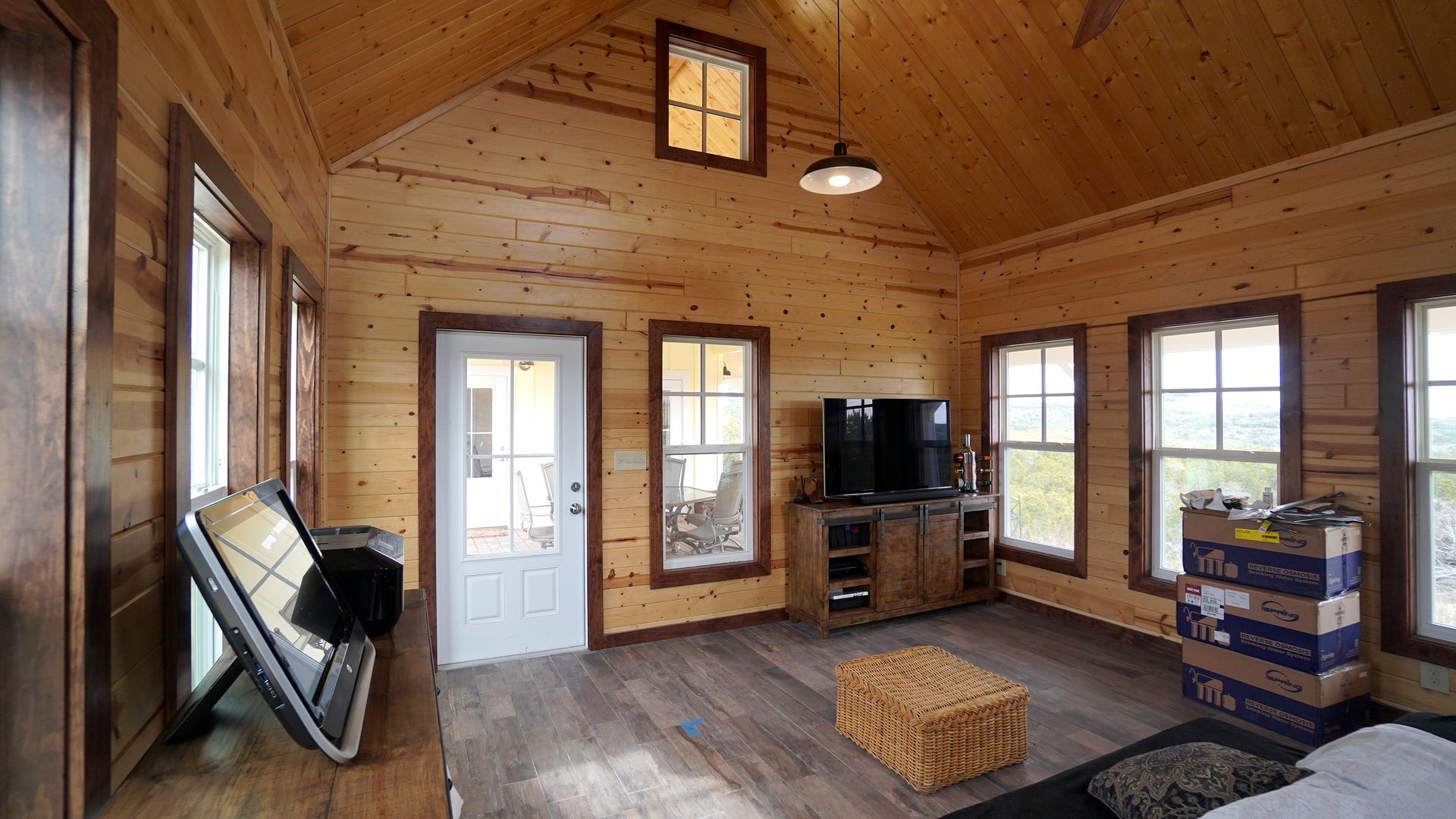 Interior of a cabin-like room with wood walls, windows, TV, and boxes.