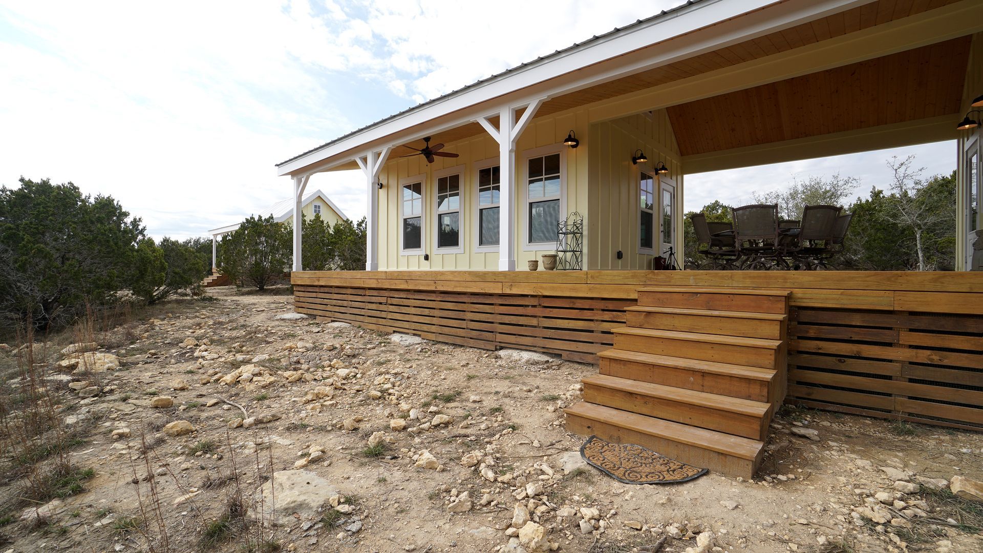 Yellow house with porch and wooden deck in a rocky, outdoor setting.