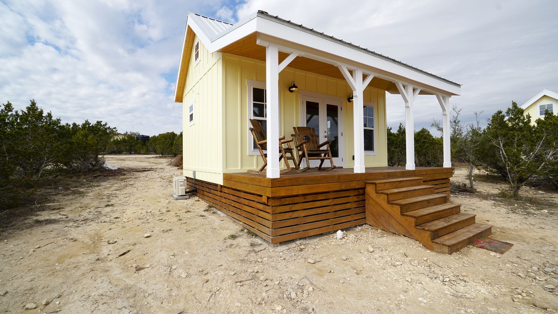 Yellow tiny house with porch and wooden steps outdoors.