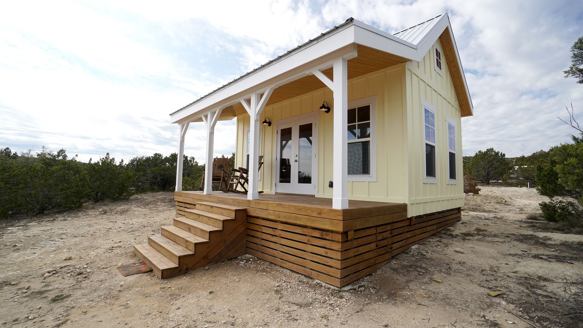 Yellow tiny house with porch and wooden steps outdoors.