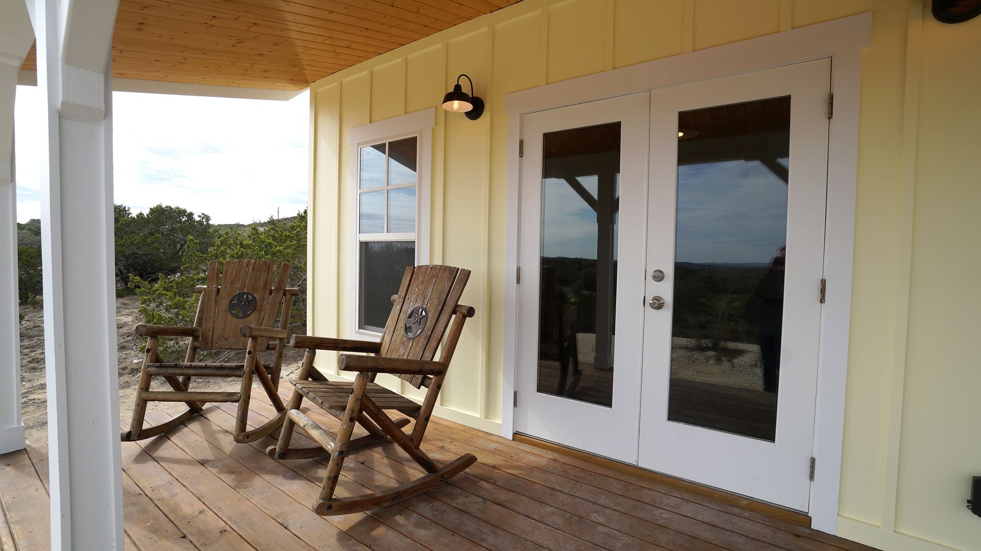 Wooden rocking chairs on a porch with French doors and windows, overlooking a rural landscape.