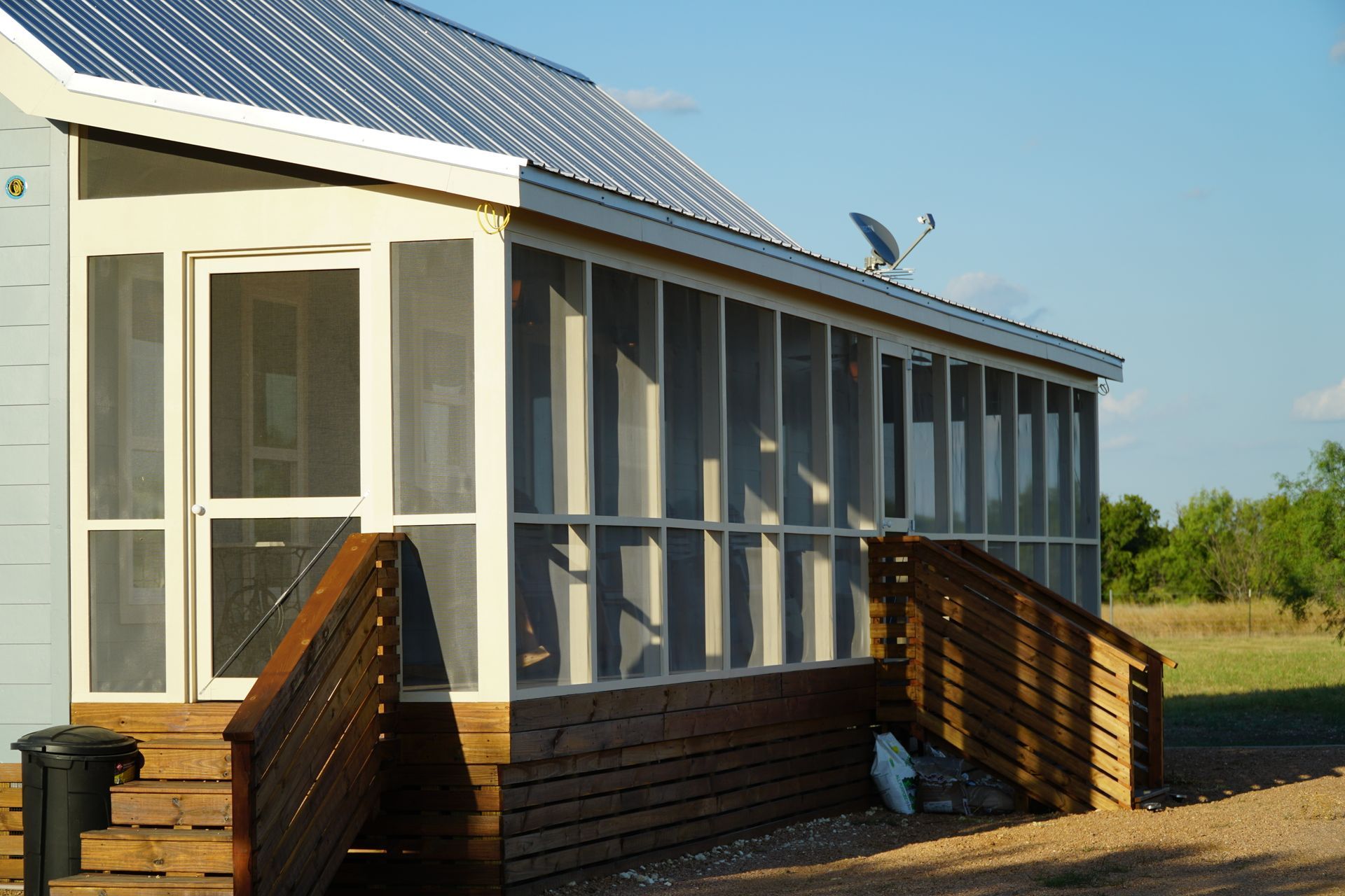 Screened-in porch attached to a light blue building, with wooden stairs, and a satellite dish.