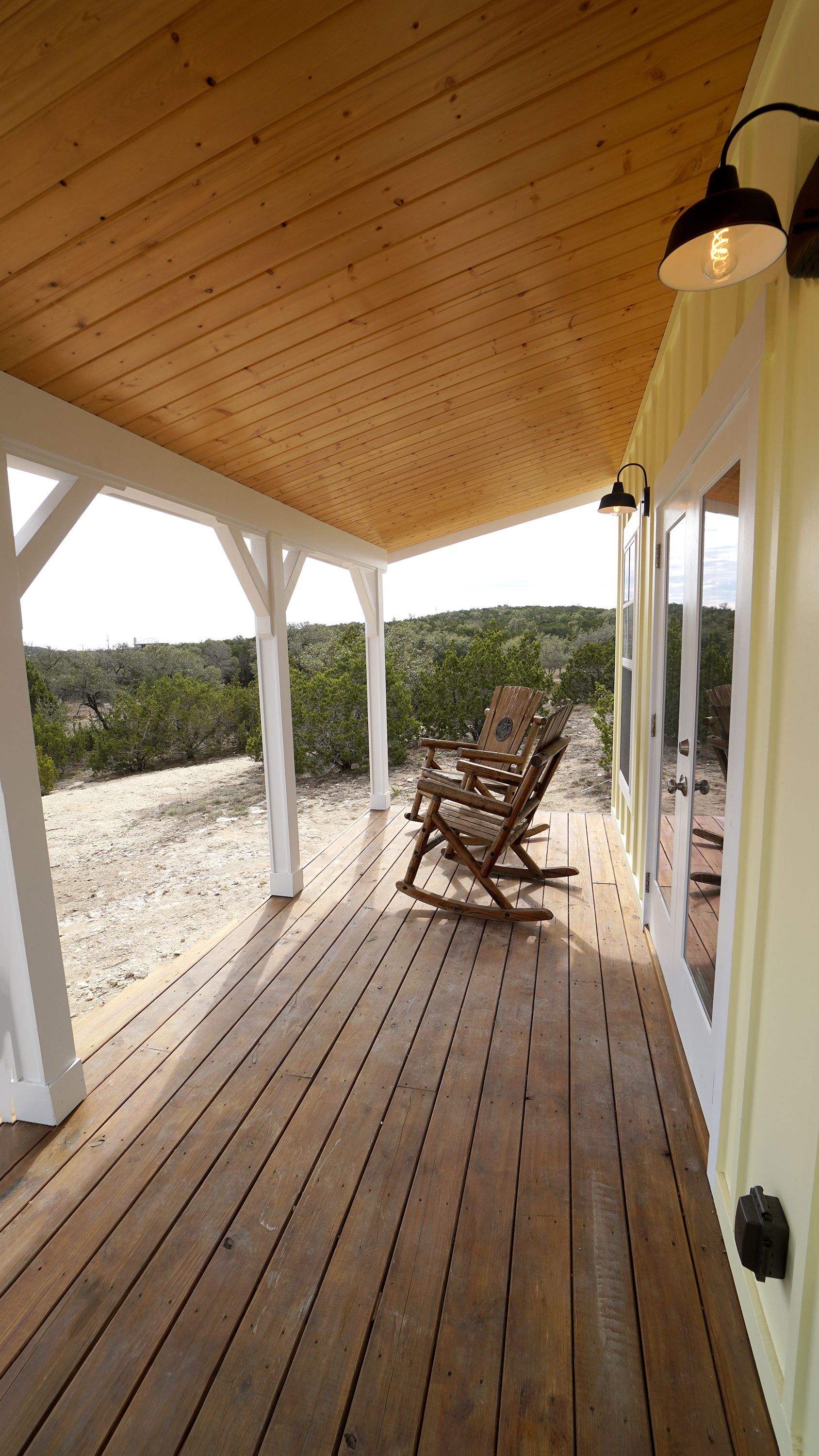 Covered porch with wood ceiling and floor, white columns, two rocking chairs, and a scenic view.