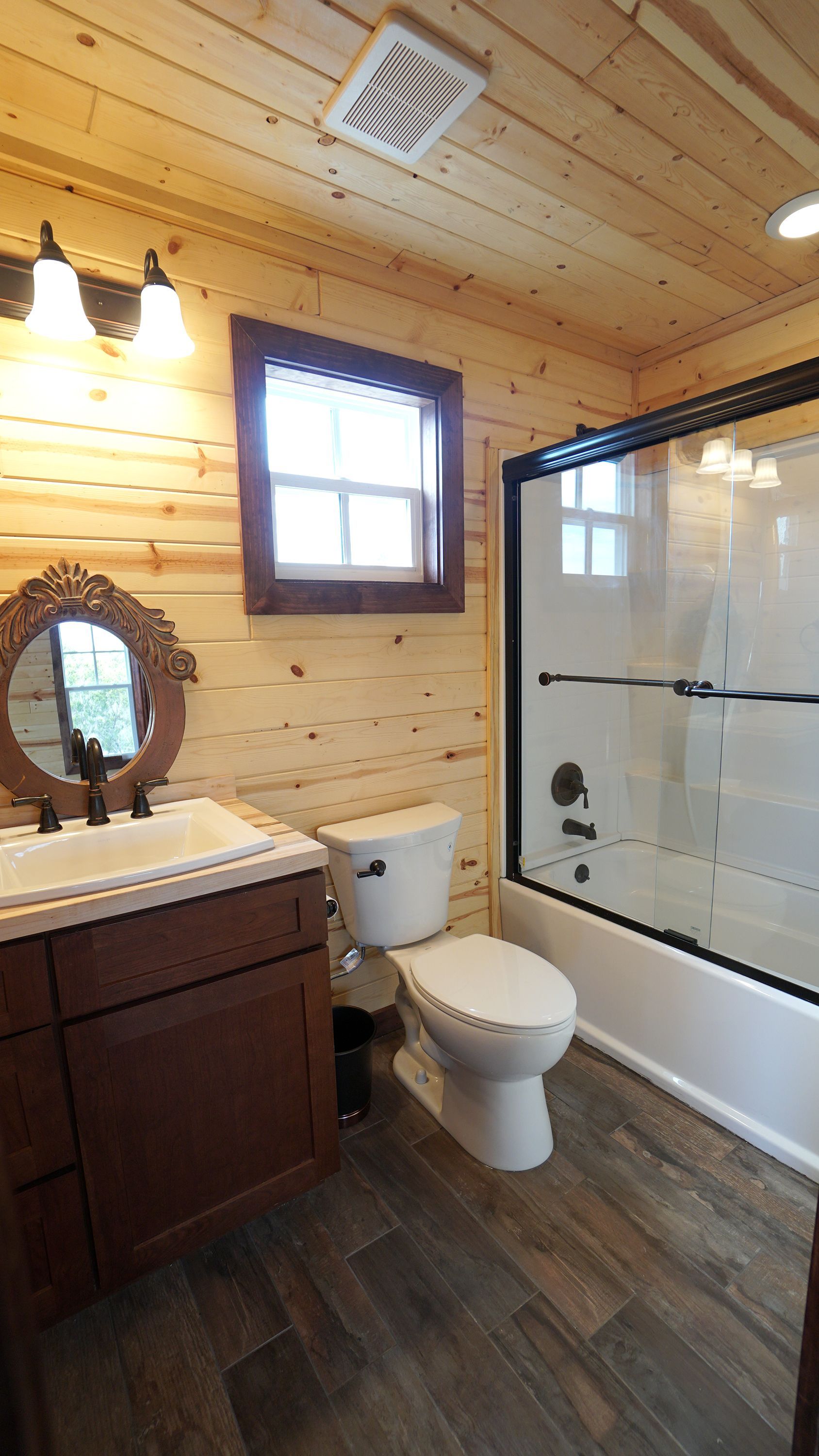 Bathroom with wood paneling, dark vanity, toilet, and shower. Brown wood-look floor, window, and mirror.