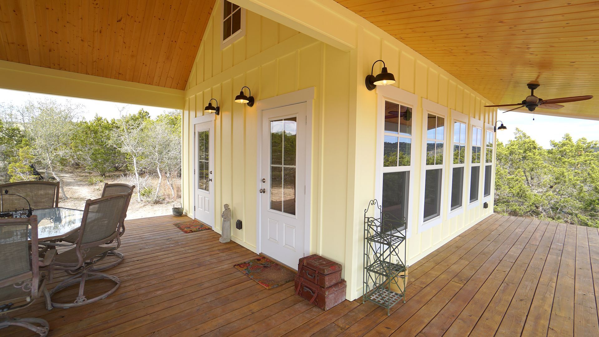 Yellow house with brown deck, doors, and windows overlooking trees.