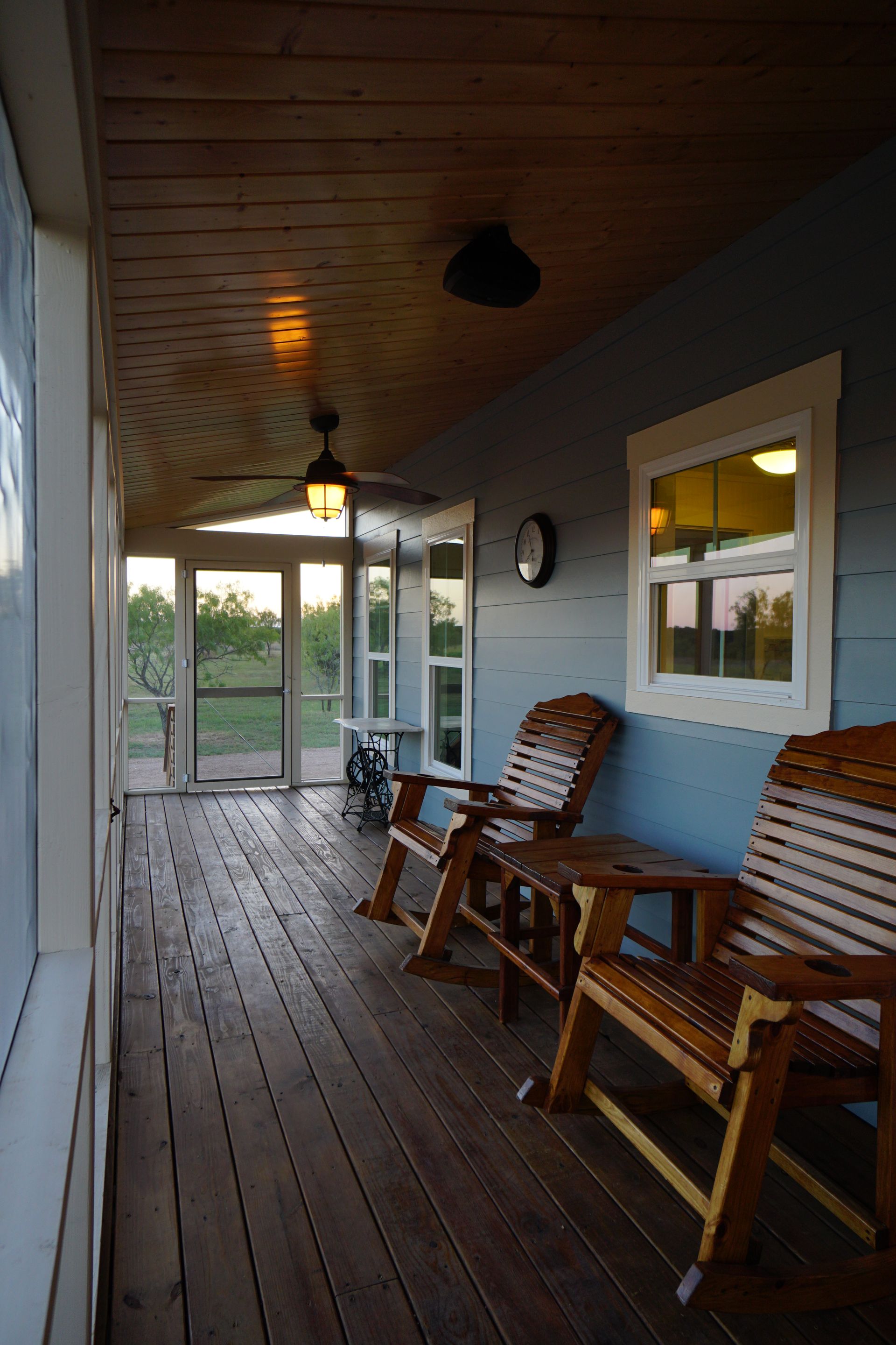 Wooden porch with rocking chairs and a screen door, overlooking a yard at dusk.