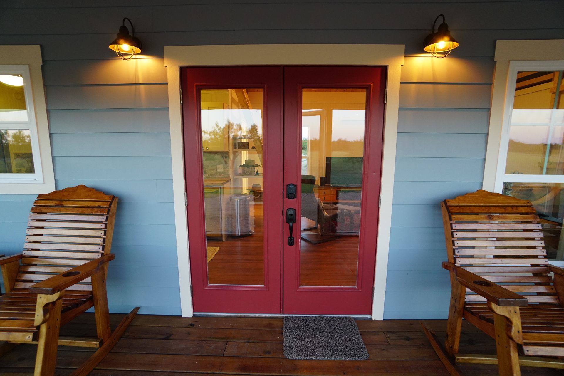 Red double doors with glass panels, flanked by rocking chairs on a blue porch, under outdoor lights.