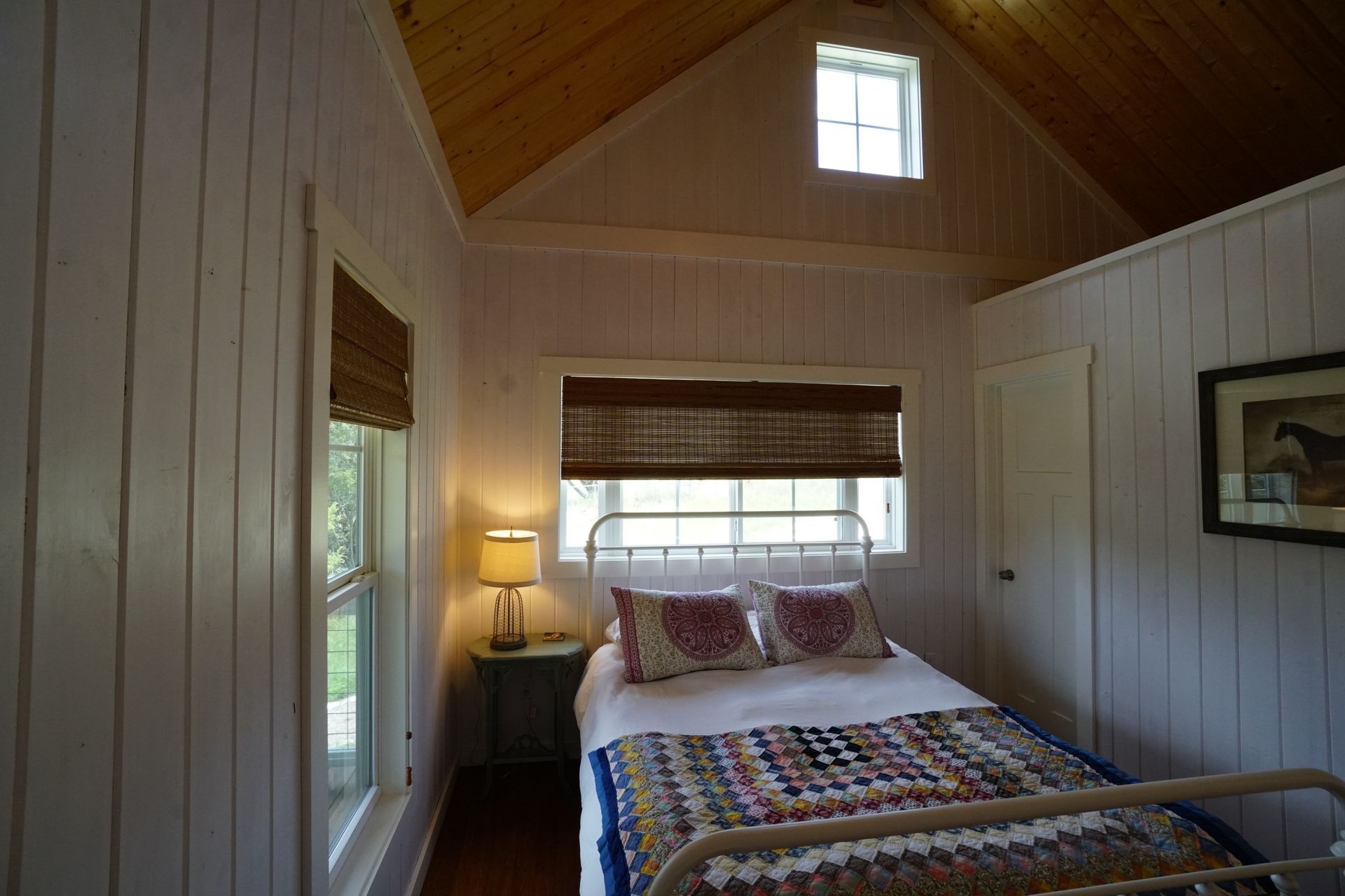 Cozy bedroom with white walls, wood ceiling, bed, windows, and decorative quilt.