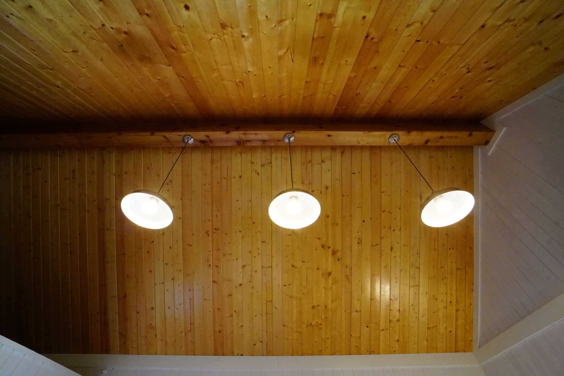 Wooden ceiling and wall with three pendant lights hanging from a horizontal beam.