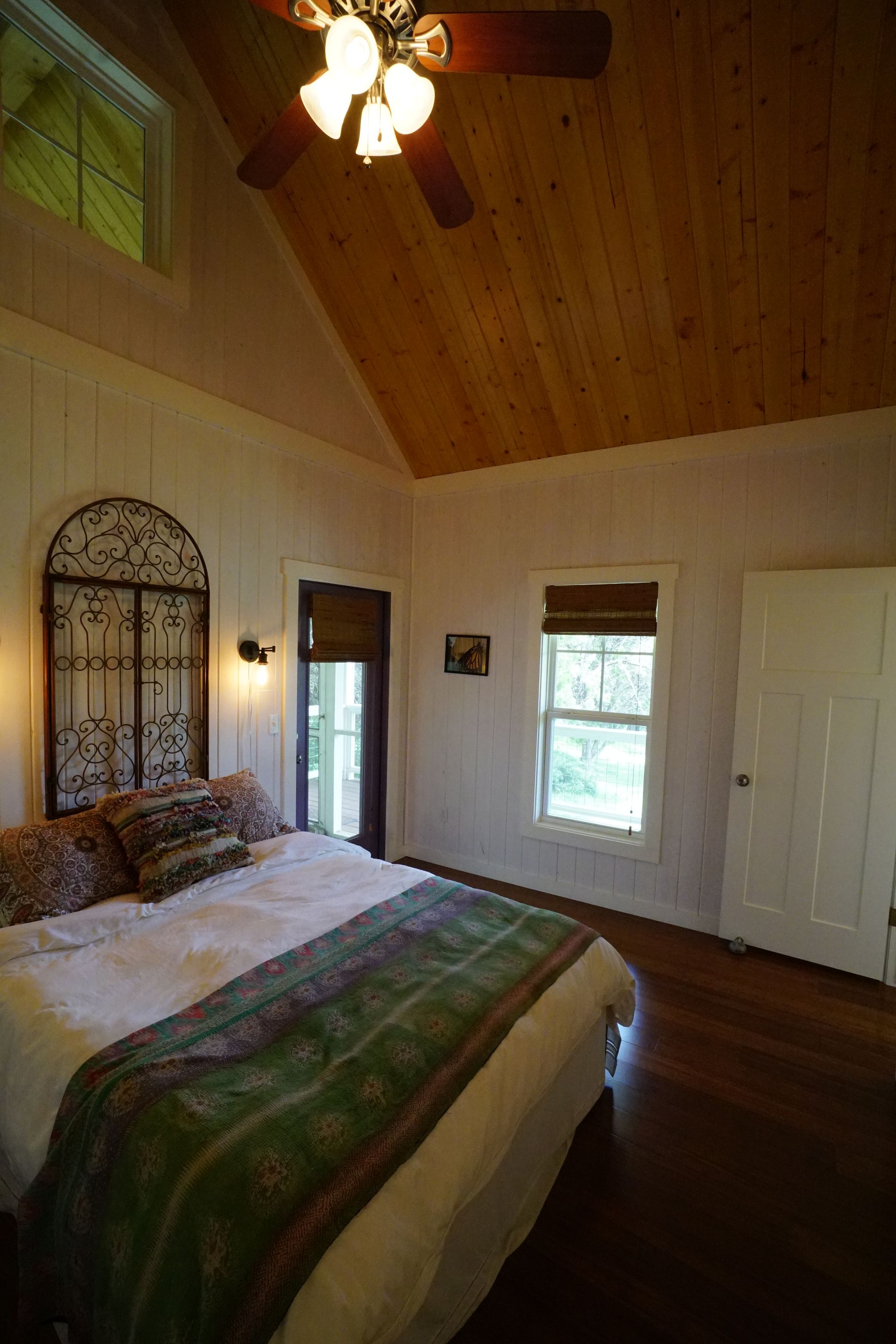 Bedroom with high ceiling, wooden floor, white walls, and a bed with green blanket.