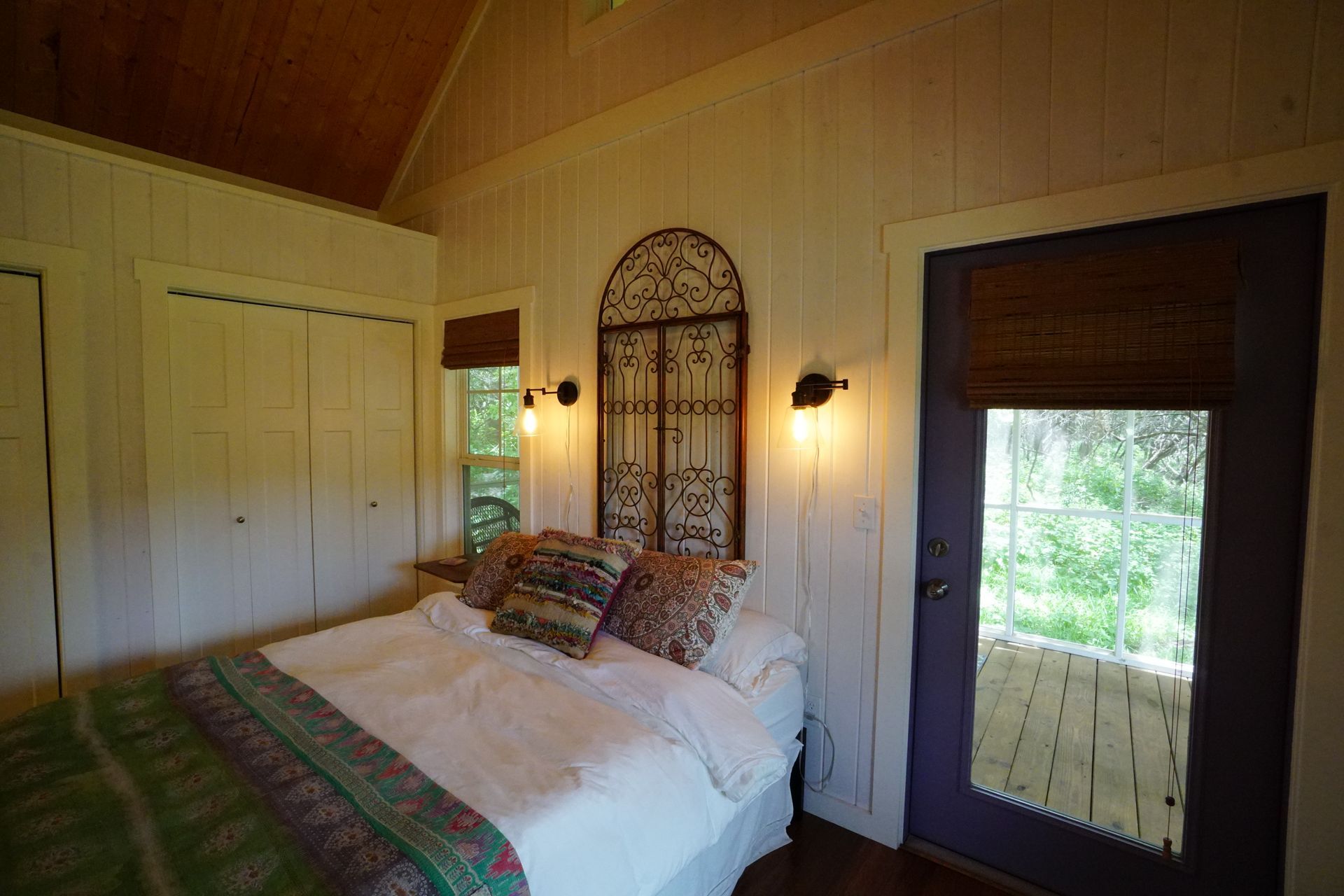 Bedroom interior with white walls, bed, door to porch, and decorative headboard.