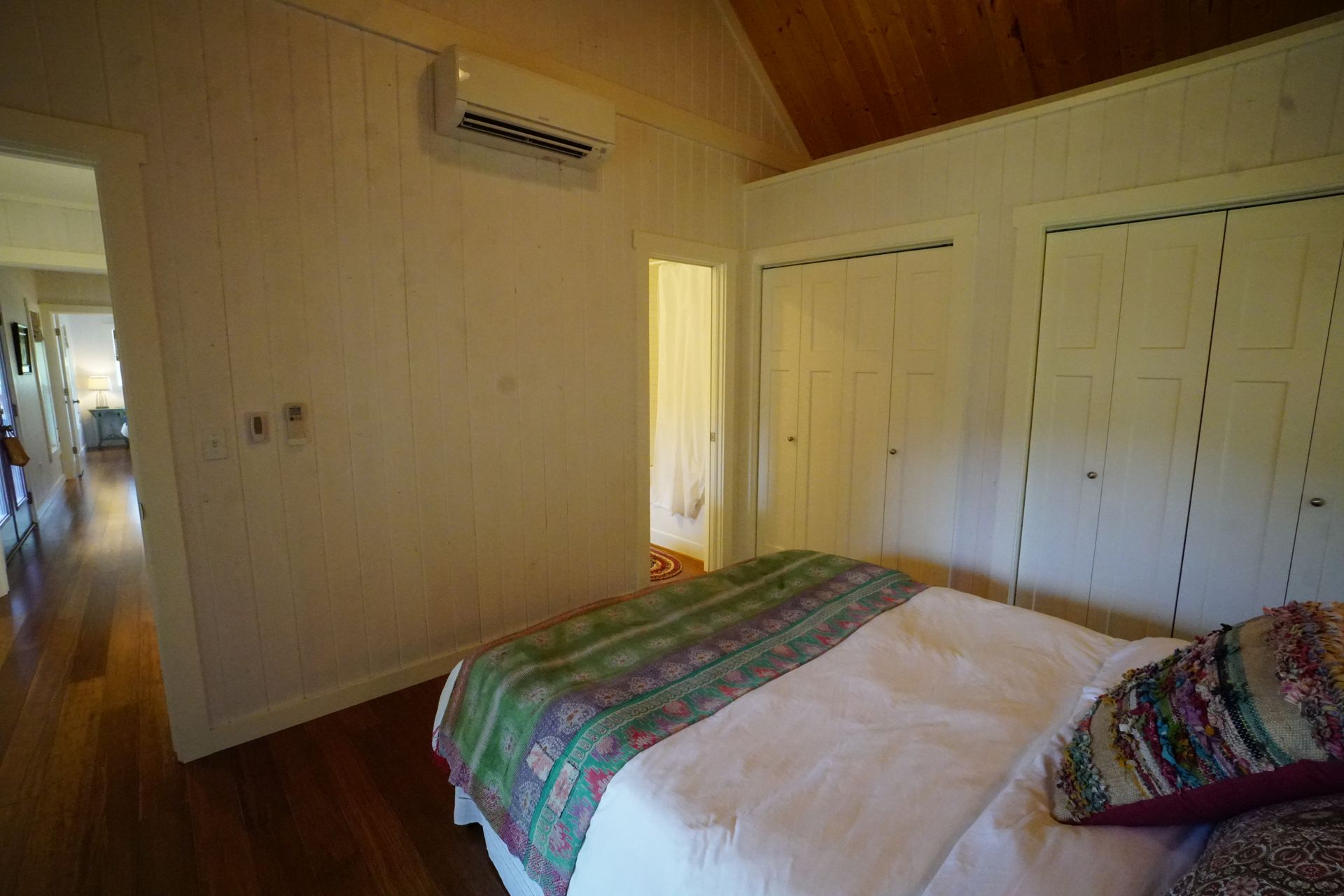 Bedroom with white walls, wood floor, bed with patterned quilt, and two closets.