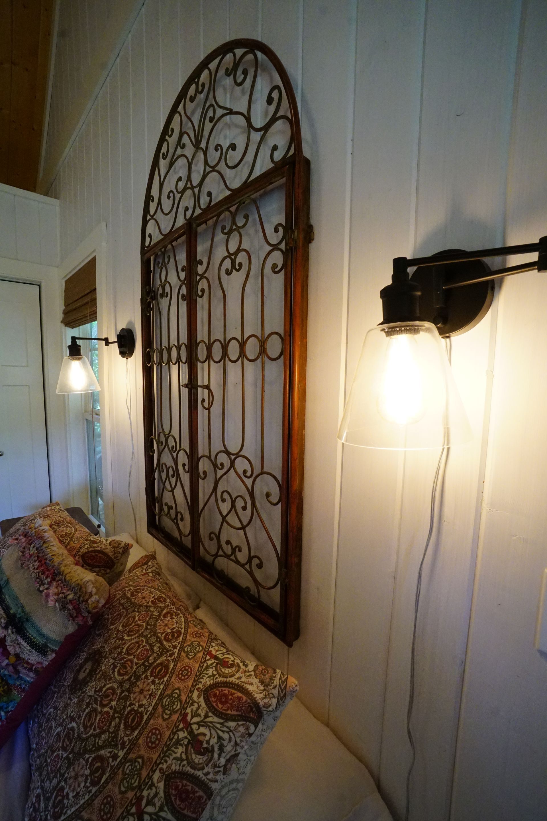 Bedside wall with decorative metalwork and two sconce lights illuminating patterned pillows.