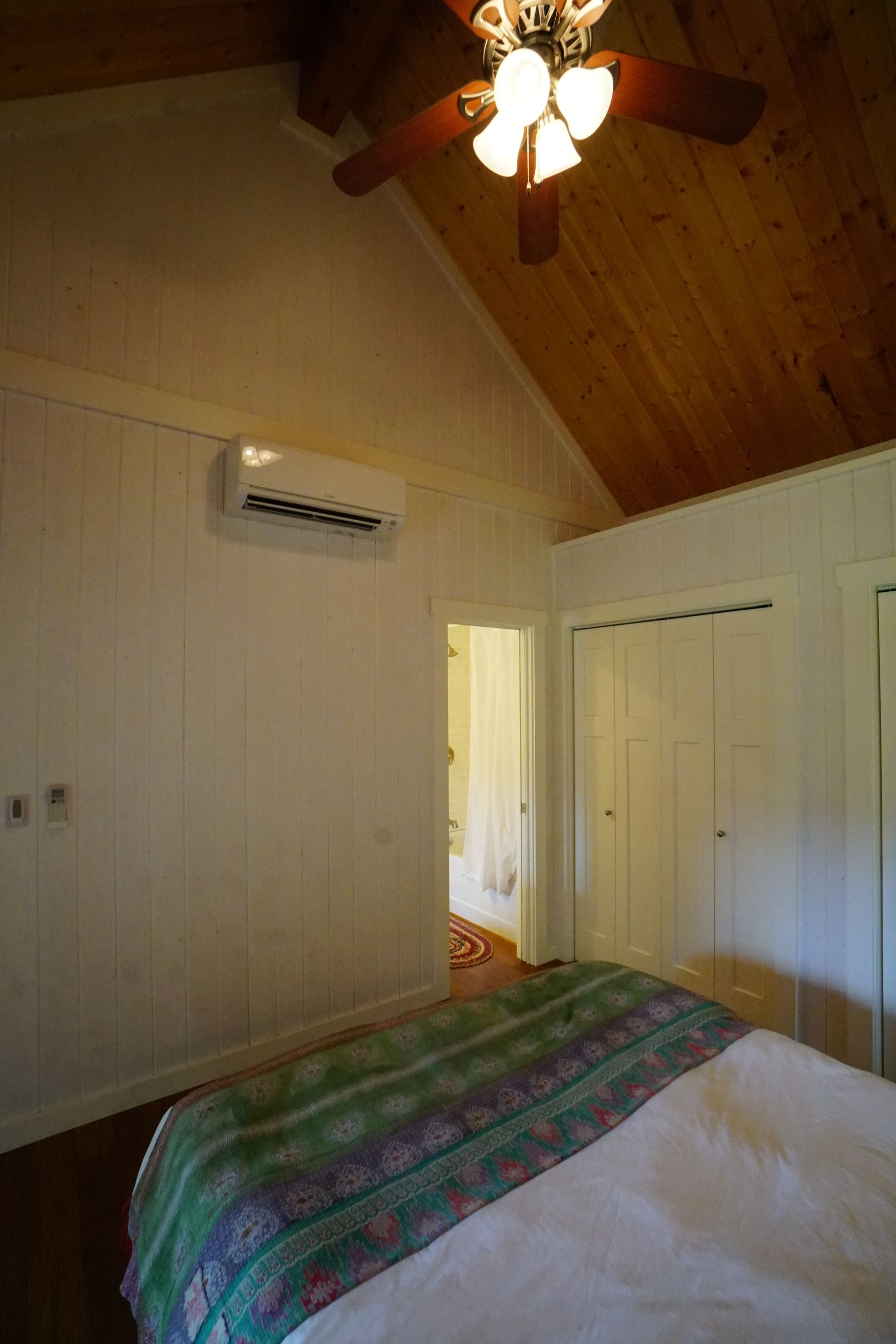 Bedroom interior with white walls, wood ceiling, bed, closets, and air conditioner unit.