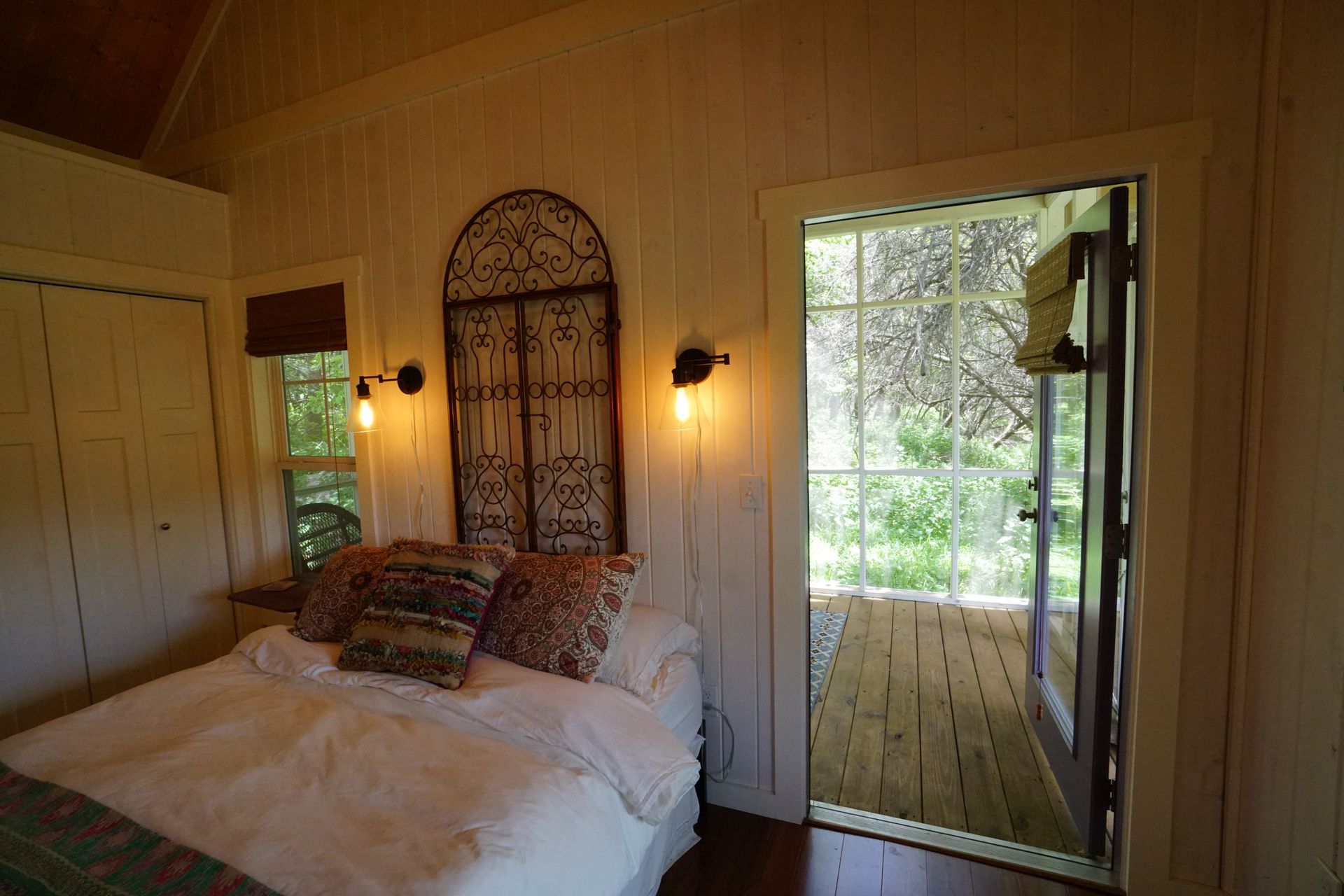 Cozy bedroom with bed, open doorway to small deck, decorative headboard, and wood-paneled walls.