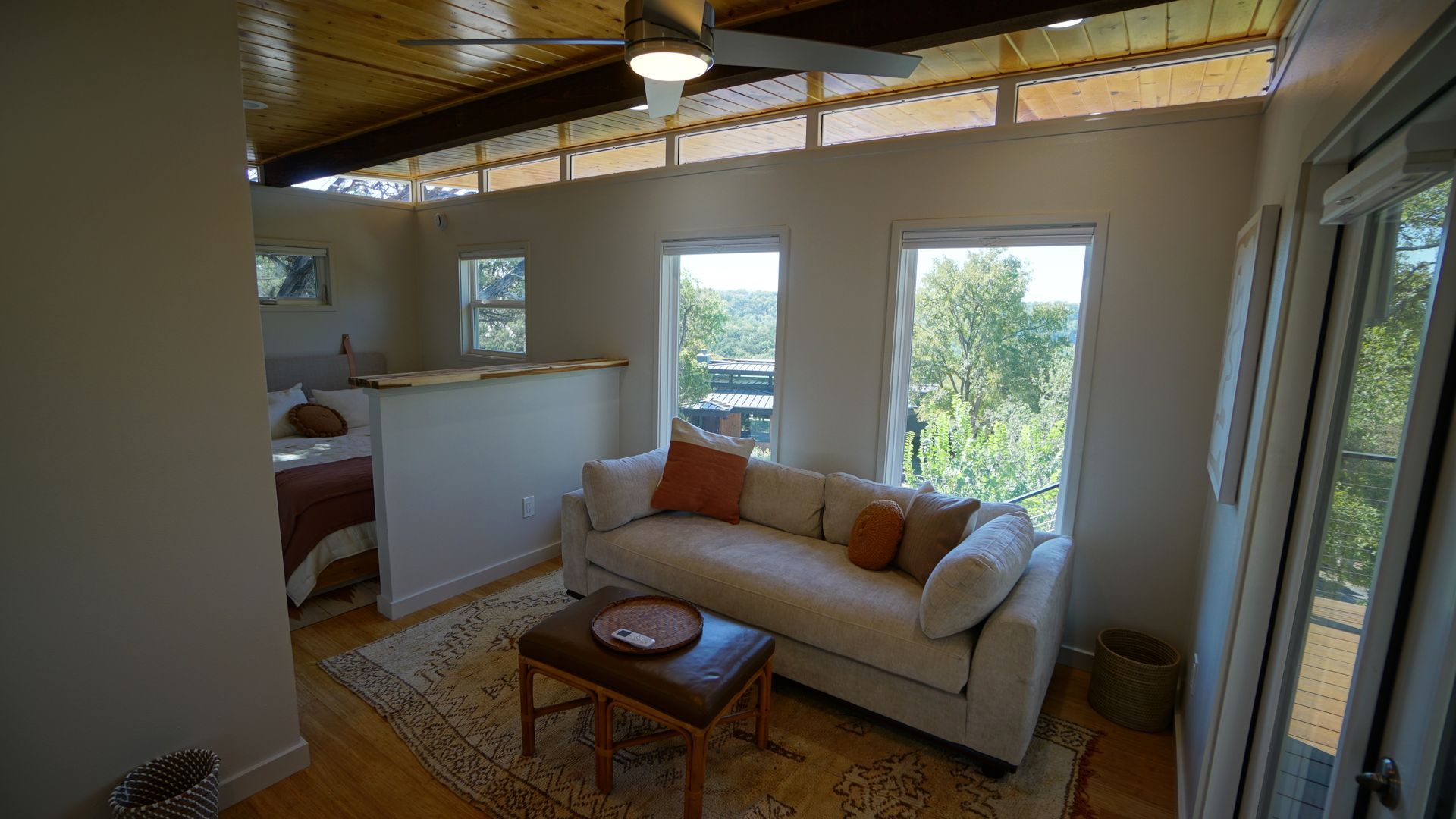 Living room with a sofa, windows overlooking trees, and a wooden ceiling.
