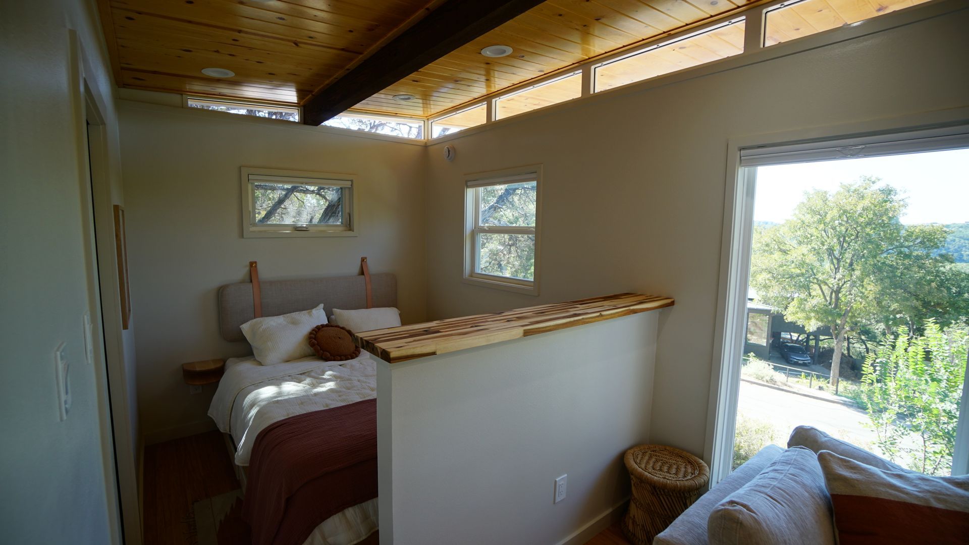 Small bedroom with bed, large window, wood ceiling, and partial wall.