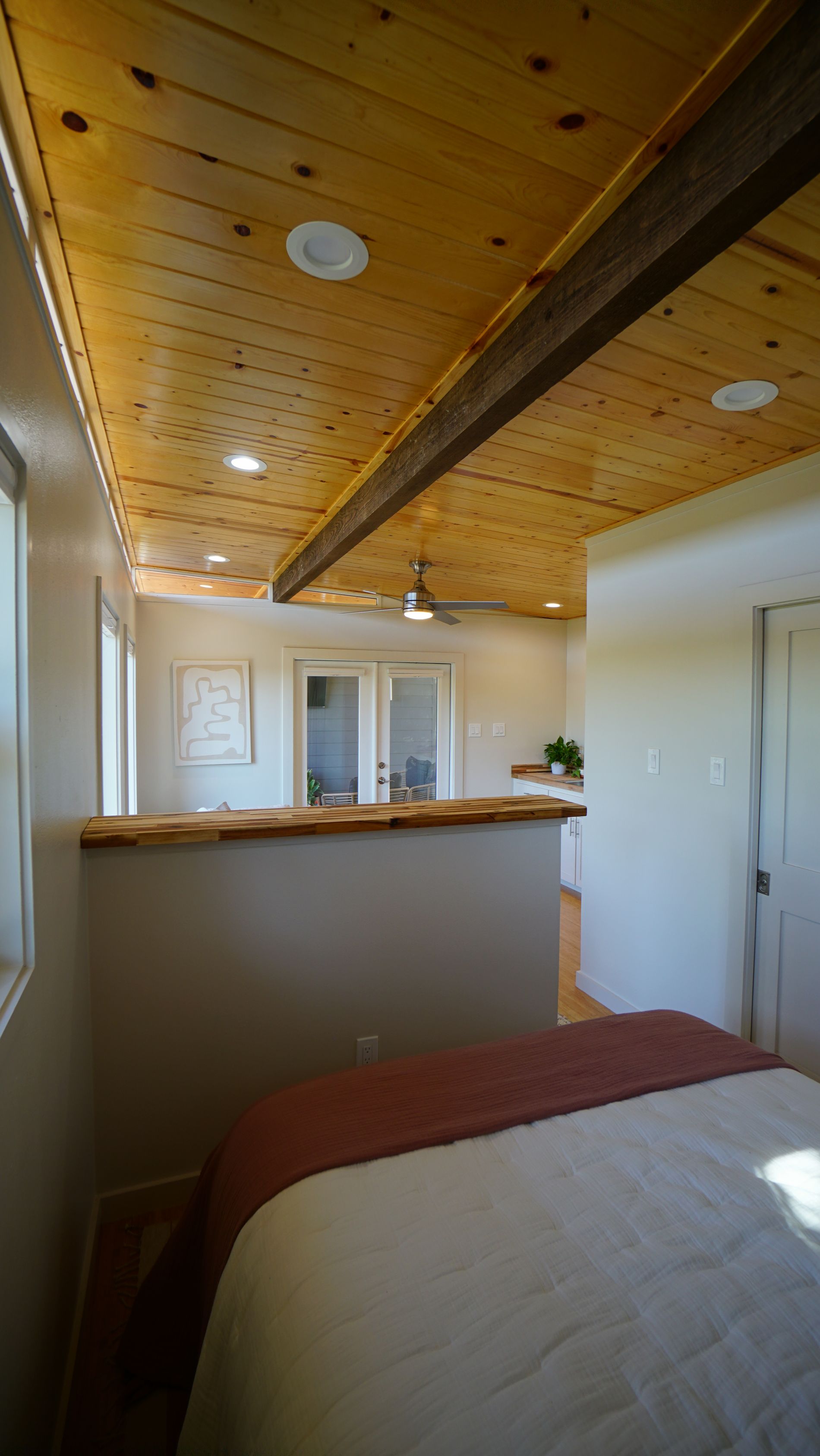 Bedroom interior with wood-plank ceiling, exposed beam, partial wall, and bed with red throw.