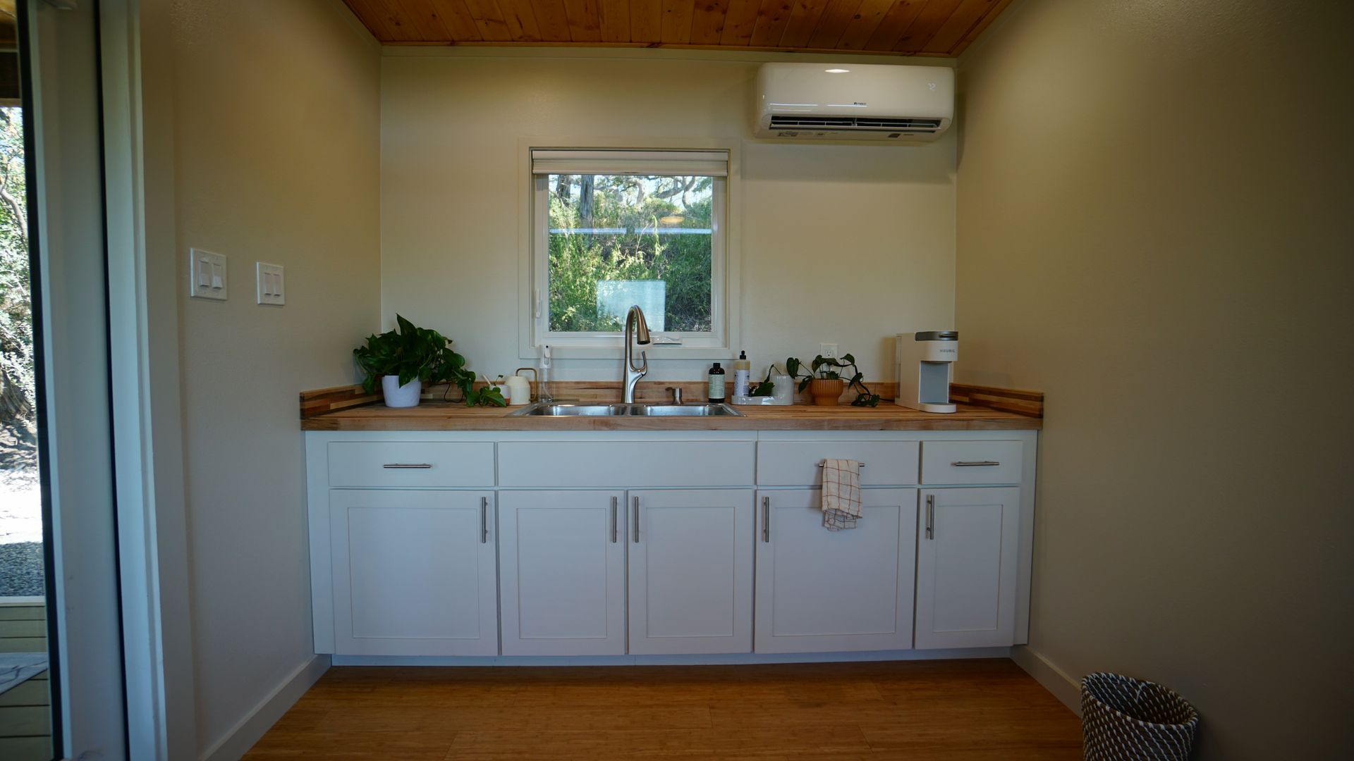 Small kitchen with white cabinets, wood countertop, sink, window, air conditioner.
