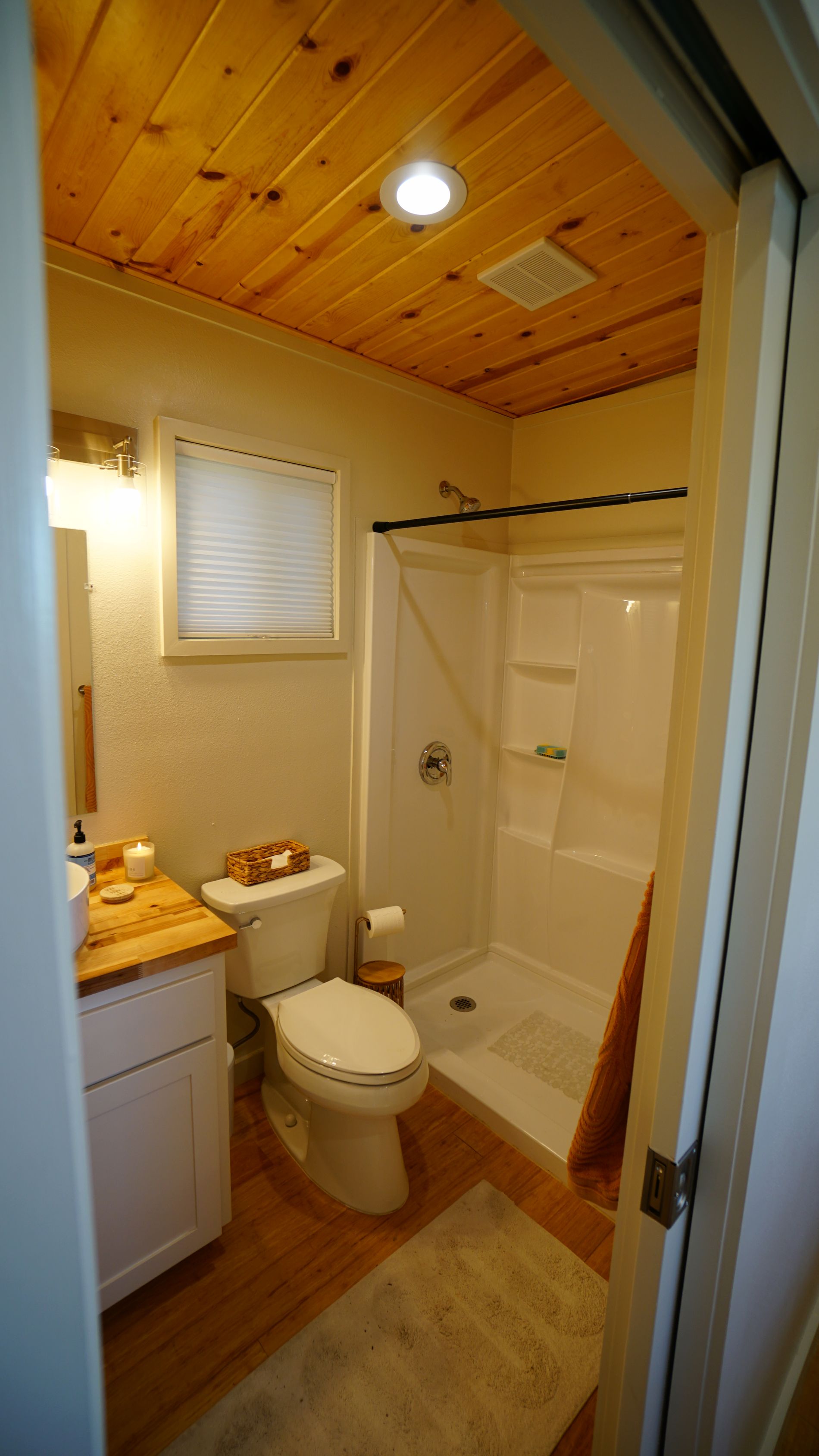 Bathroom interior with wood ceiling, white shower, and toilet; view from doorway.