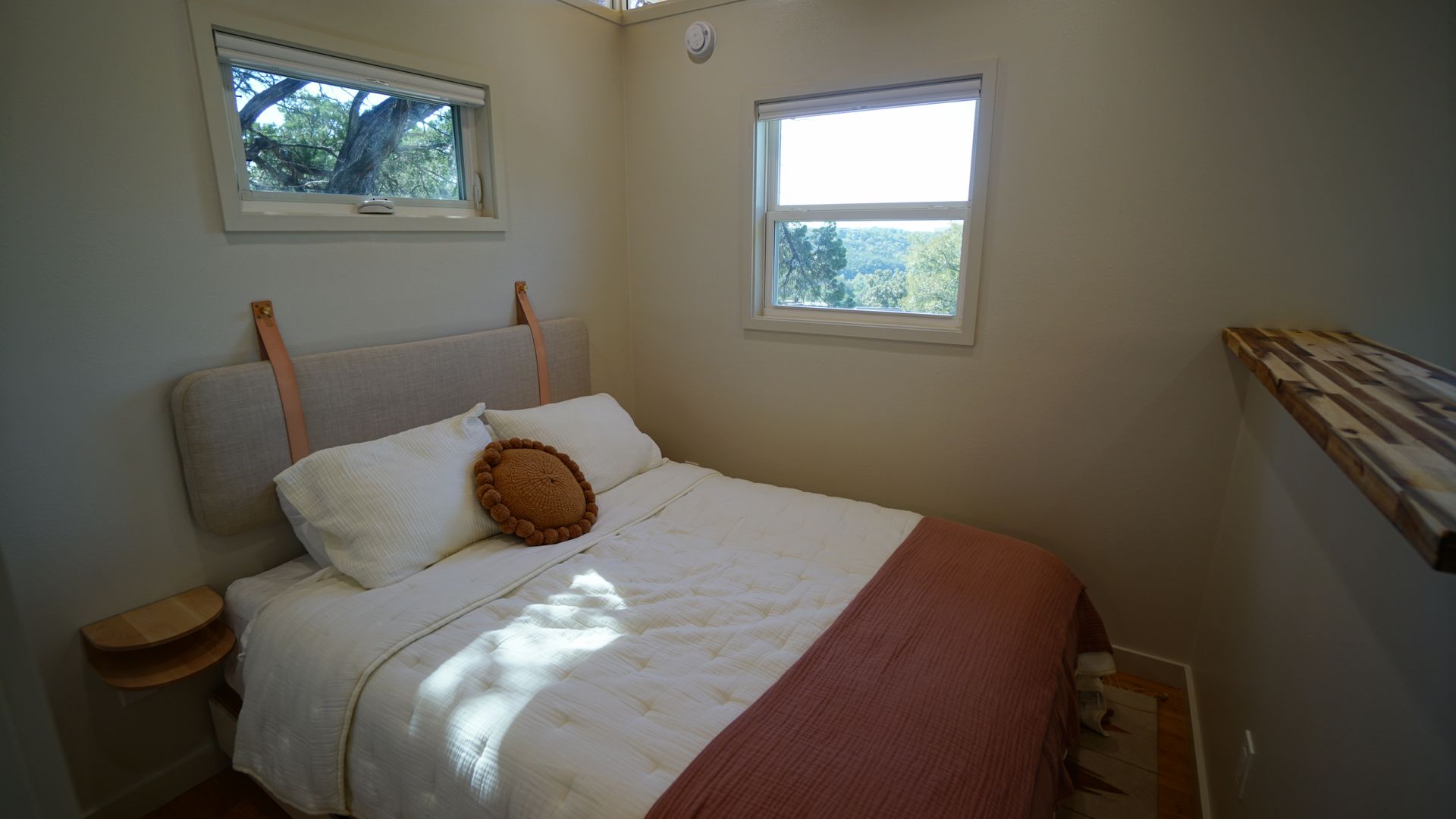 Small bedroom with bed, two windows, and side table. Natural light and neutral colors.